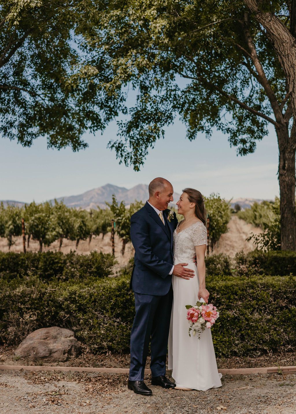 Romantic moment captured under tree branches in scenic vineyard setting.