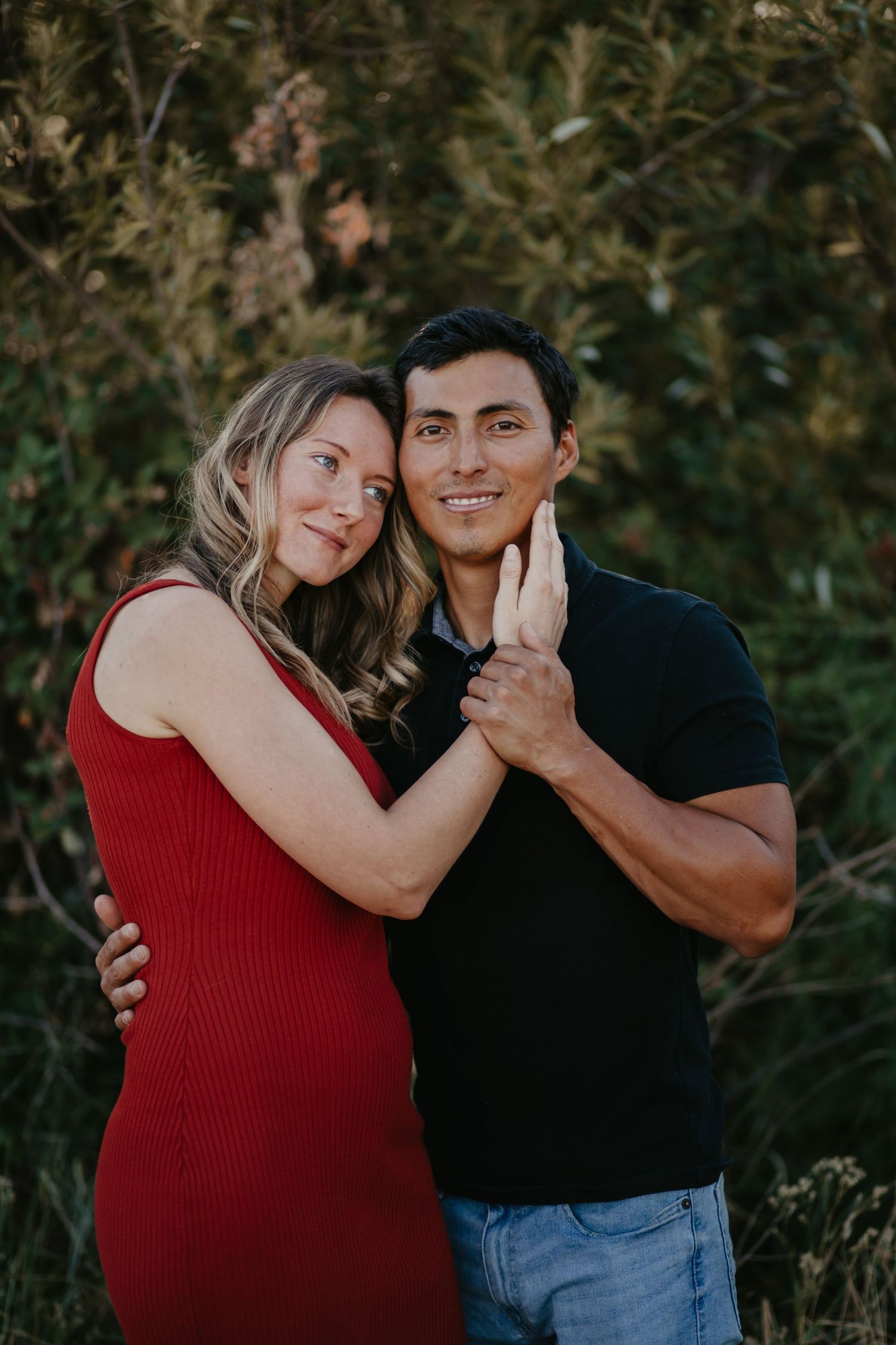A couple shares a tender moment while posing for photos outdoors in casual clothing.