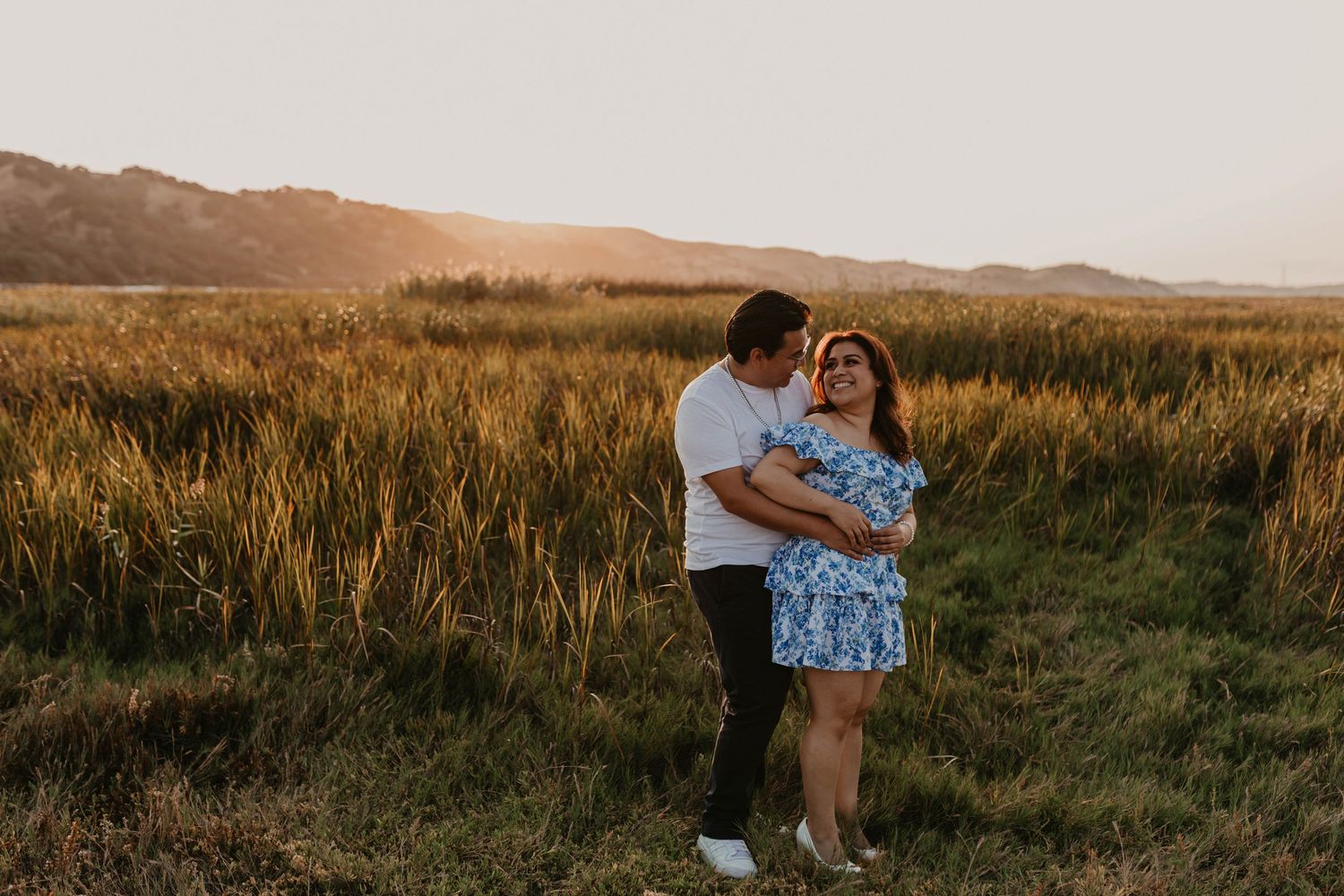 A romantic outdoor photoshoot in a grassy field during golden hour.