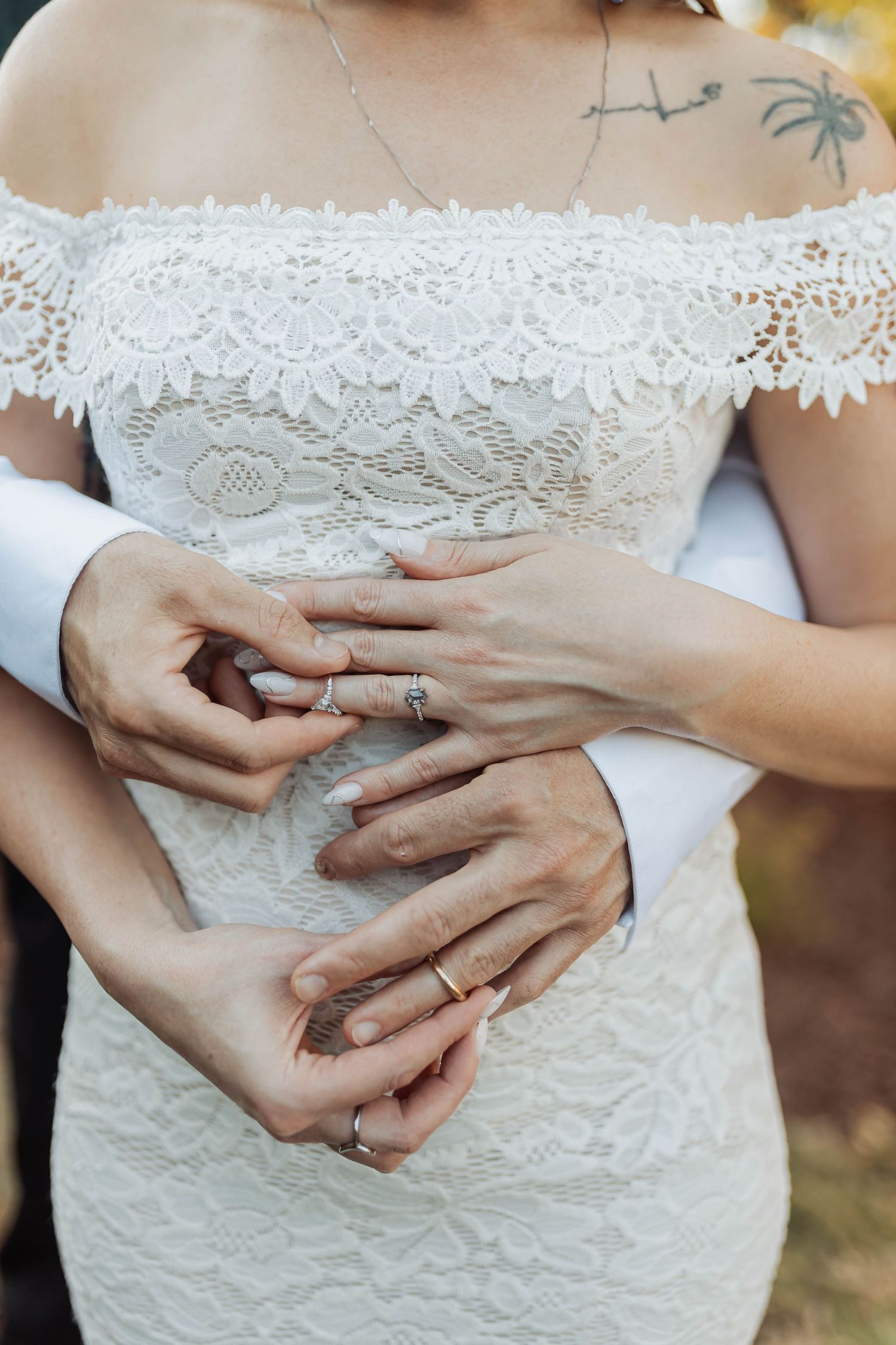 Close-up shots of wedding rings and hands against a delicate white lace wedding dress.