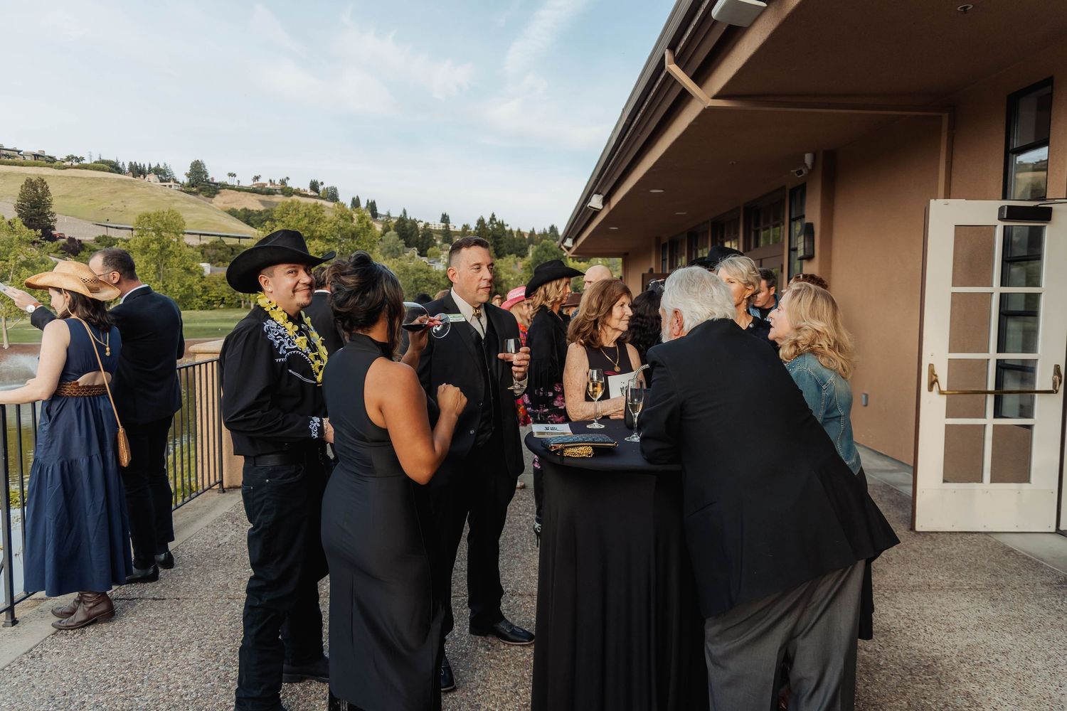 Elegant outdoor wedding reception guests mingling in formal black attire at a scenic venue with rolling hills.
