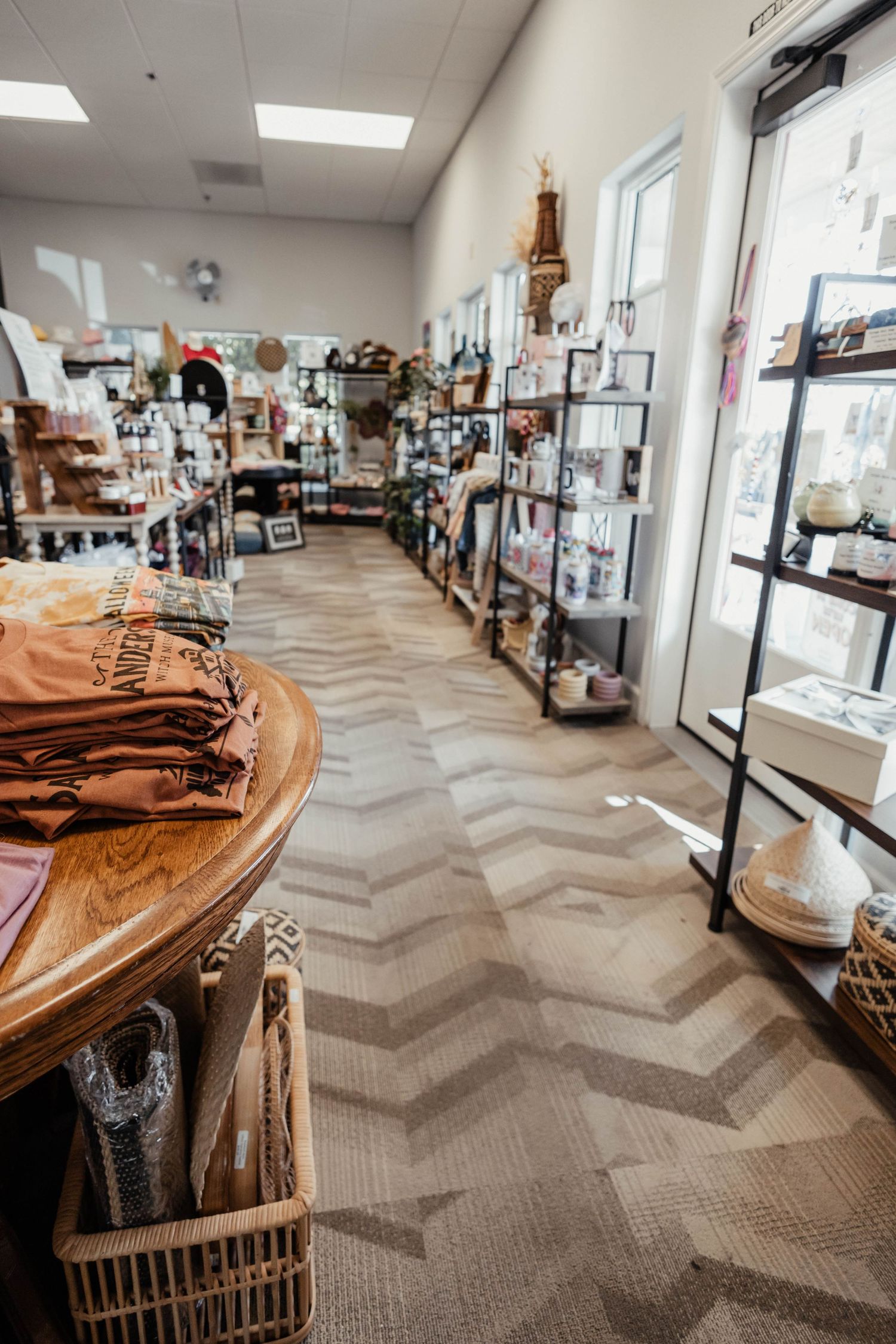 Long view of a boutique shop with chevron flooring, wooden tables, and shelves filled with merchandise.