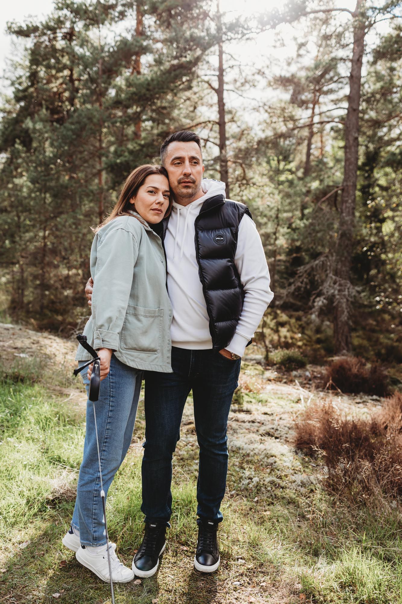 A cozy couple embracing while wearing puffy vests in a scenic forest setting.