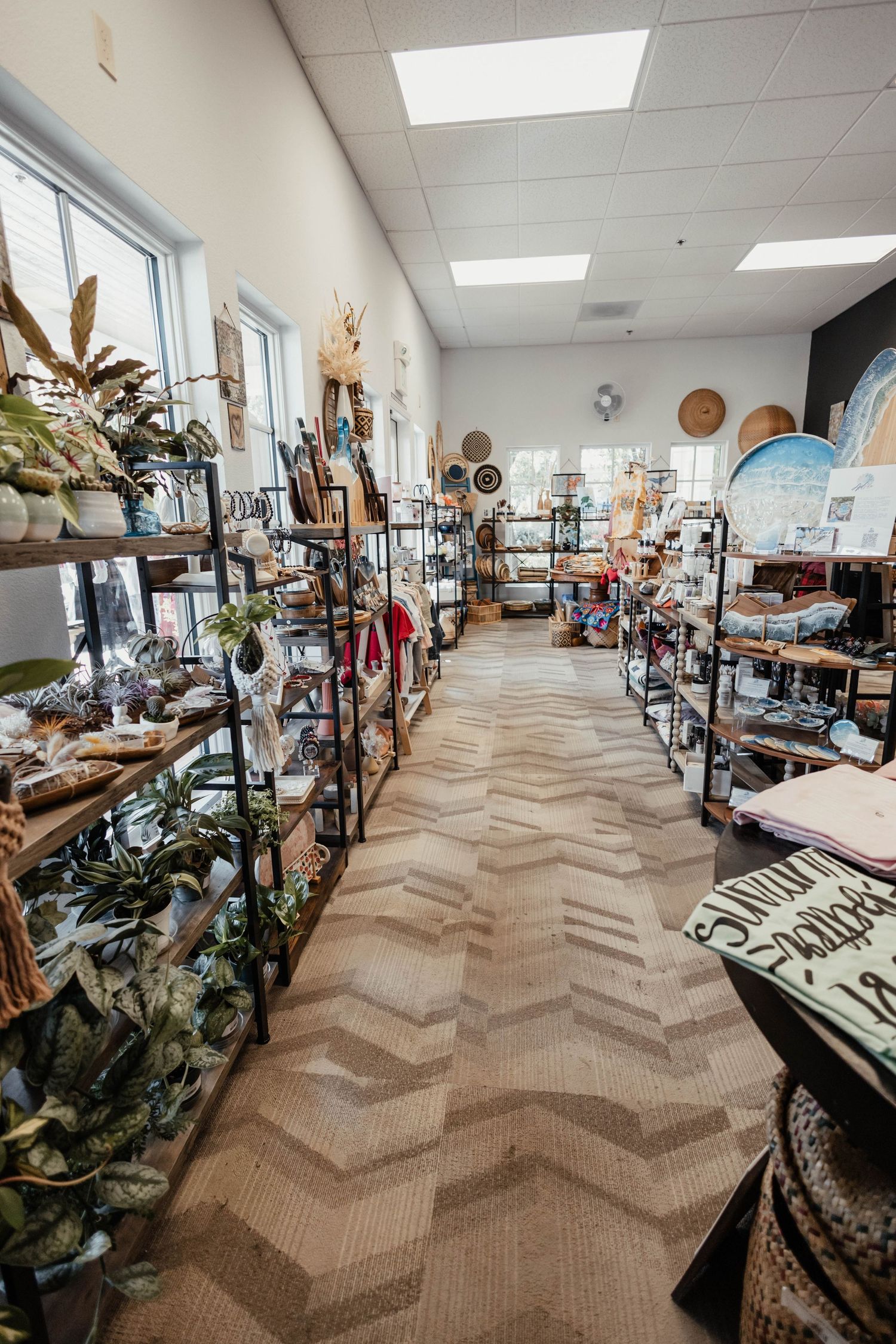 Long view of retail store interior with shelving displaying houseplants and home decor items.