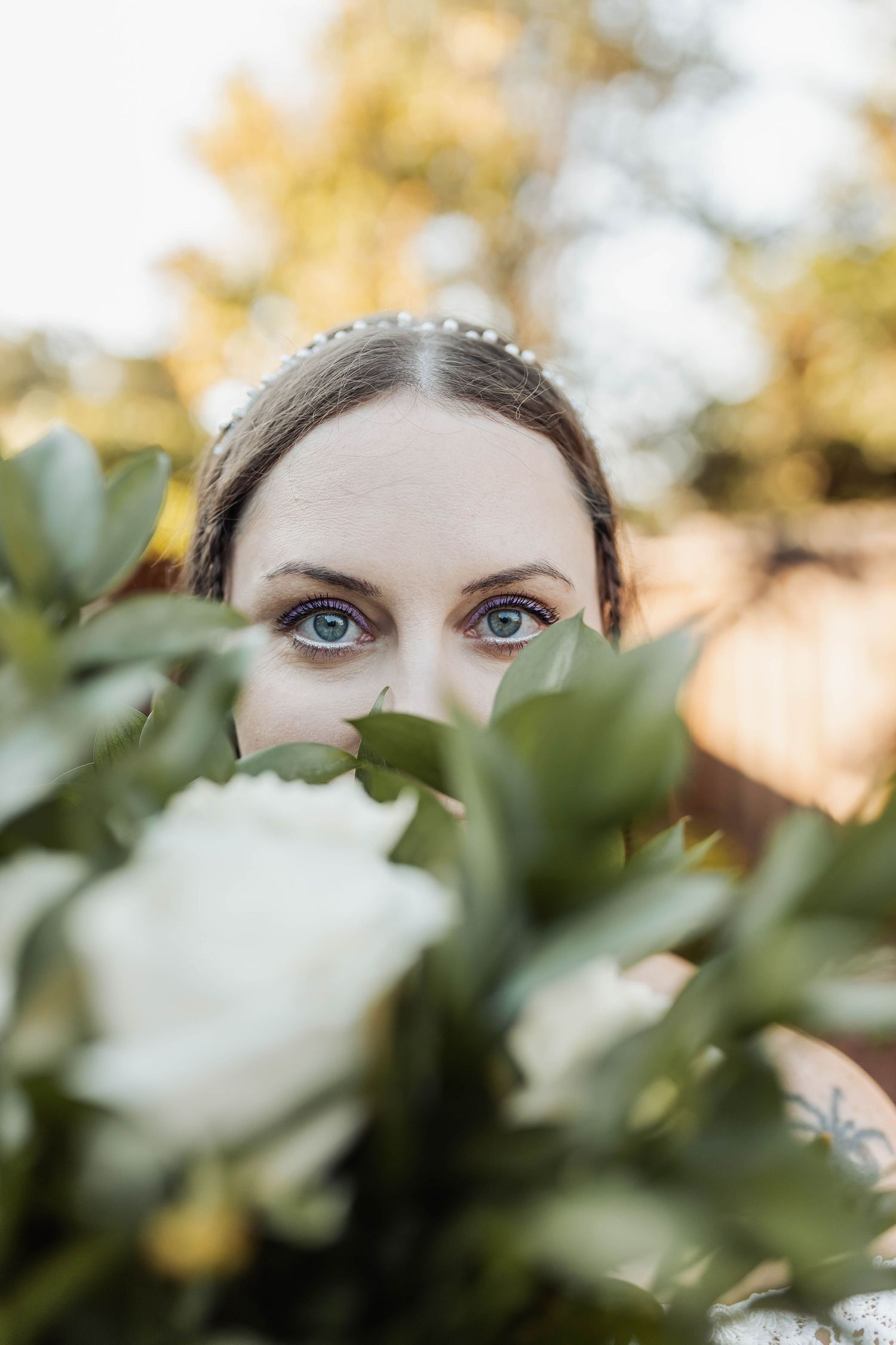 Artistic wedding photo showing eyes peeking through white flowers and green foliage.