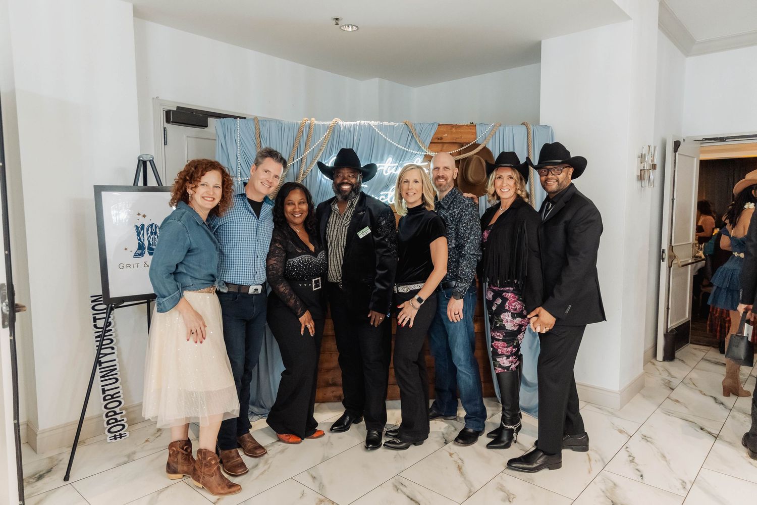 Group of nine people posing together indoors at a country-themed event, dressed in denim and cowboy hats.