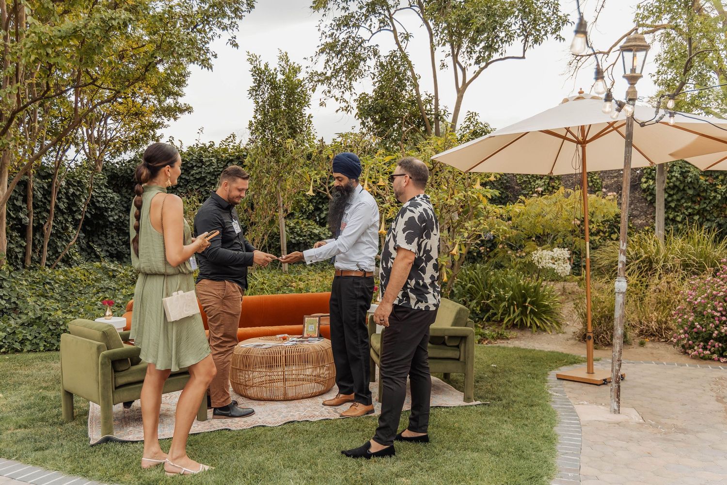 Four people networking outdoors on a garden patio, shaking hands near elegant furniture and a patio umbrella.
