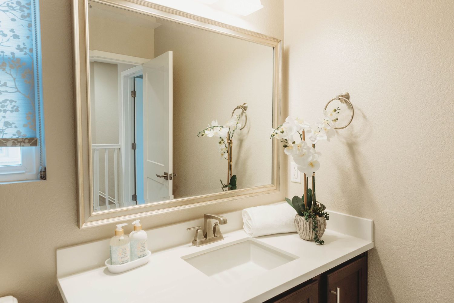 Elegant bathroom vanity with large framed mirror, white countertop, and orchid decoration.