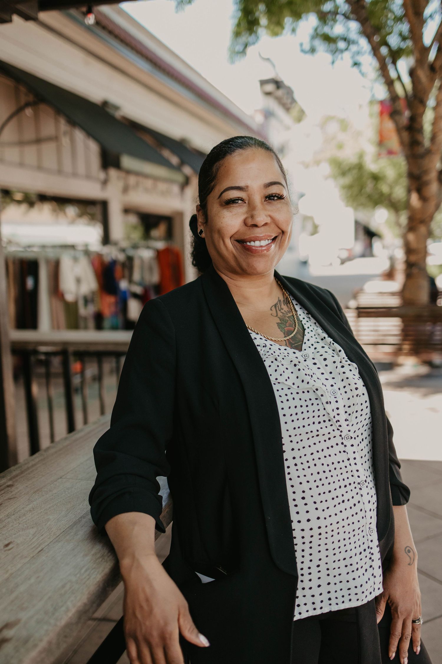 Professional business portraits showing confident poses in a black blazer and polka dot top against an outdoor backdrop.