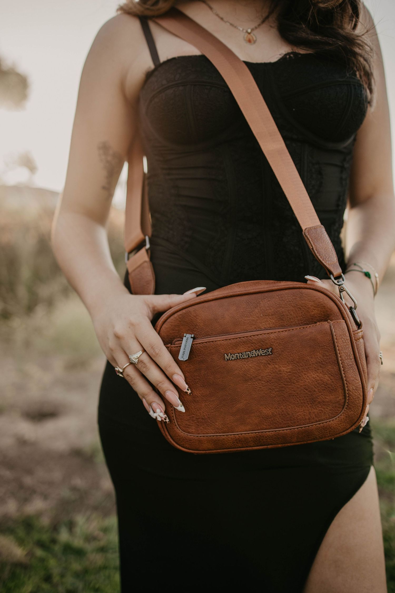 Brown leather crossbody bag styled with black dress in outdoor setting.