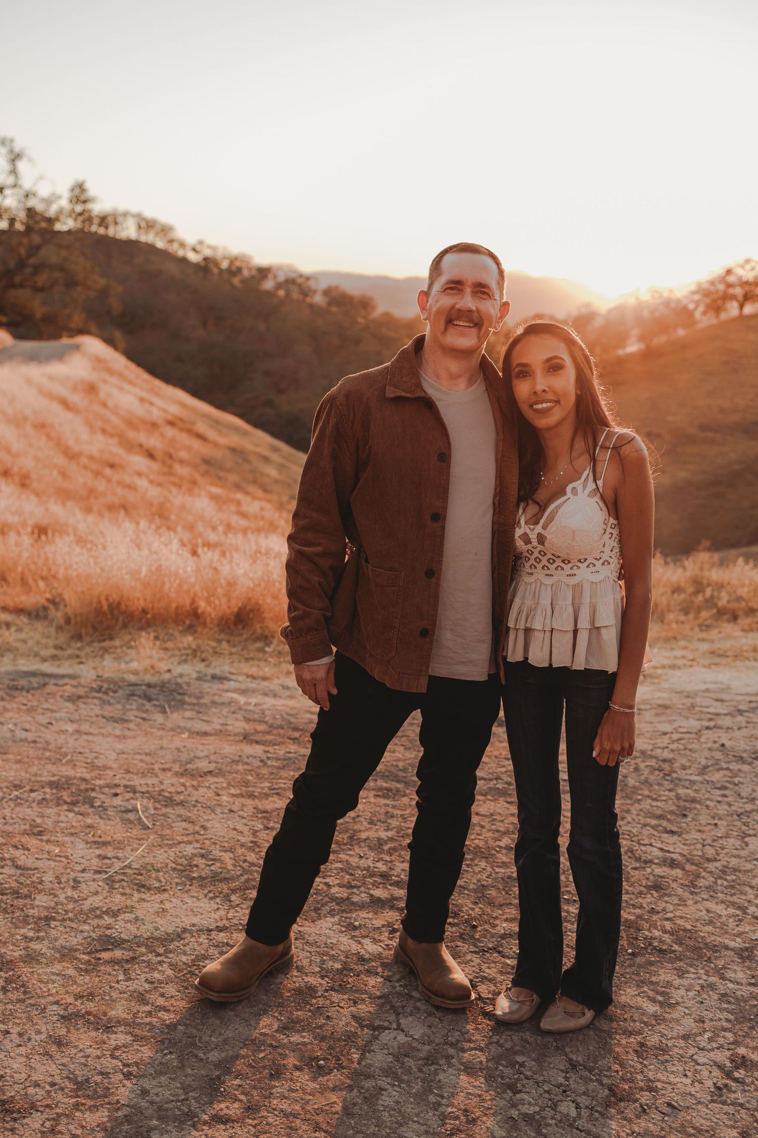 Couple standing together on hilltop path at sunset.