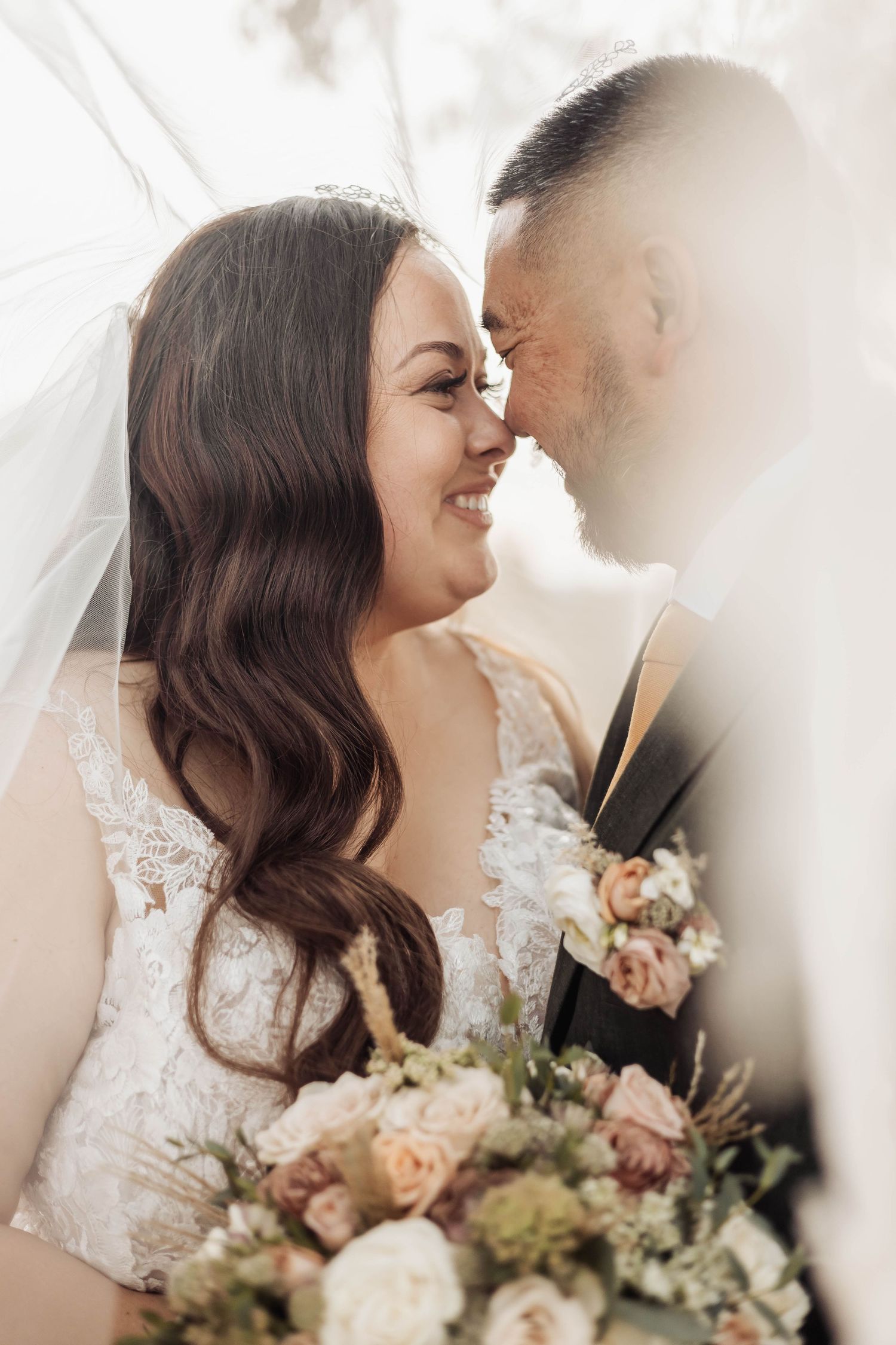 Romantic wedding portrait with white veil and blush-toned floral bouquet in soft lighting.