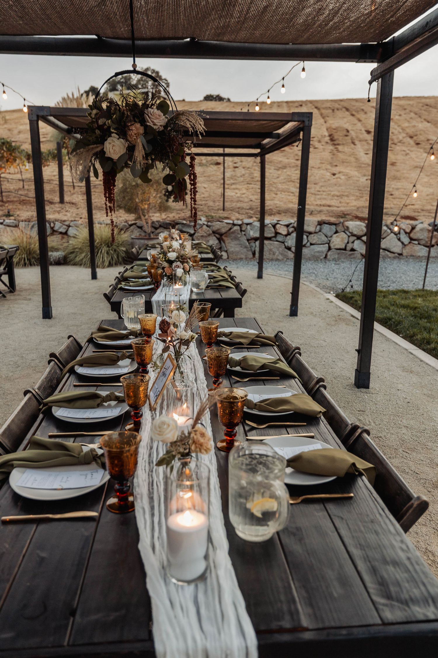 Rustic outdoor wedding reception table with dark wood and elegant place settings.