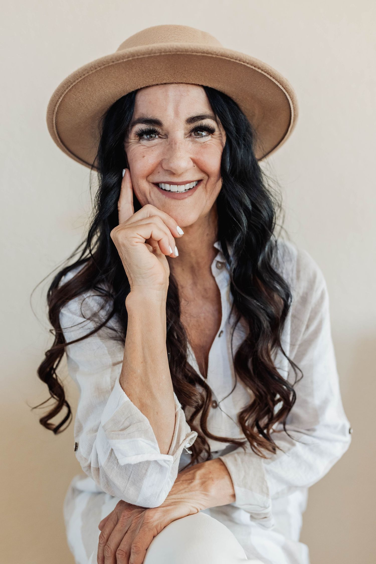 Portrait of a woman wearing a tan hat and white shirt against a neutral background.