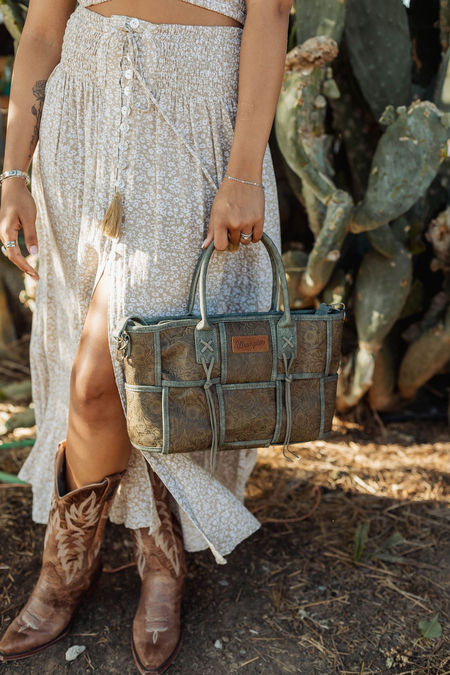 Brown leather handbag and cowboy boots styled with white floral dress near cactus garden.