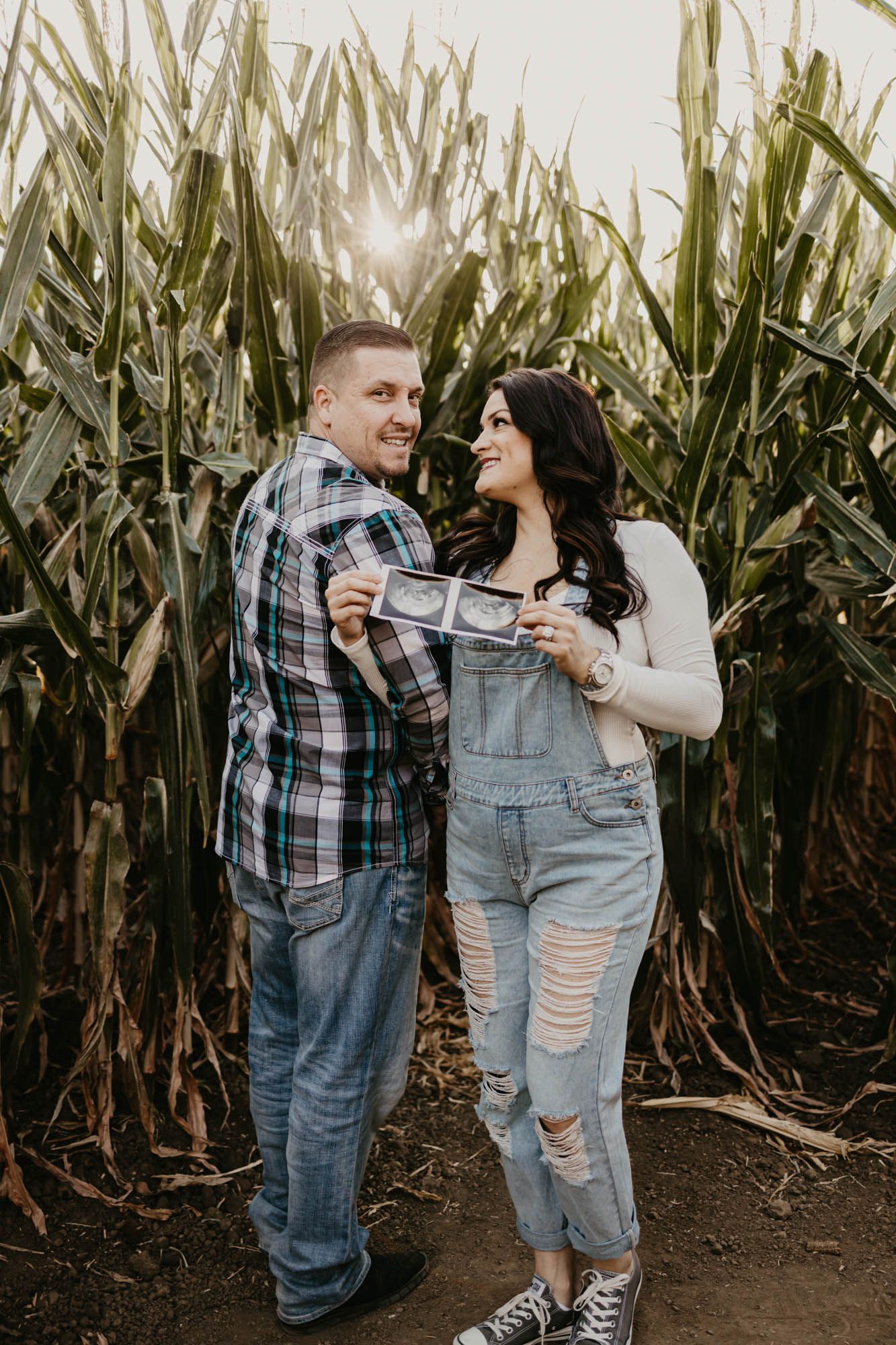 Couple sharing joyful moment while showing ultrasound pictures in front of corn stalks.