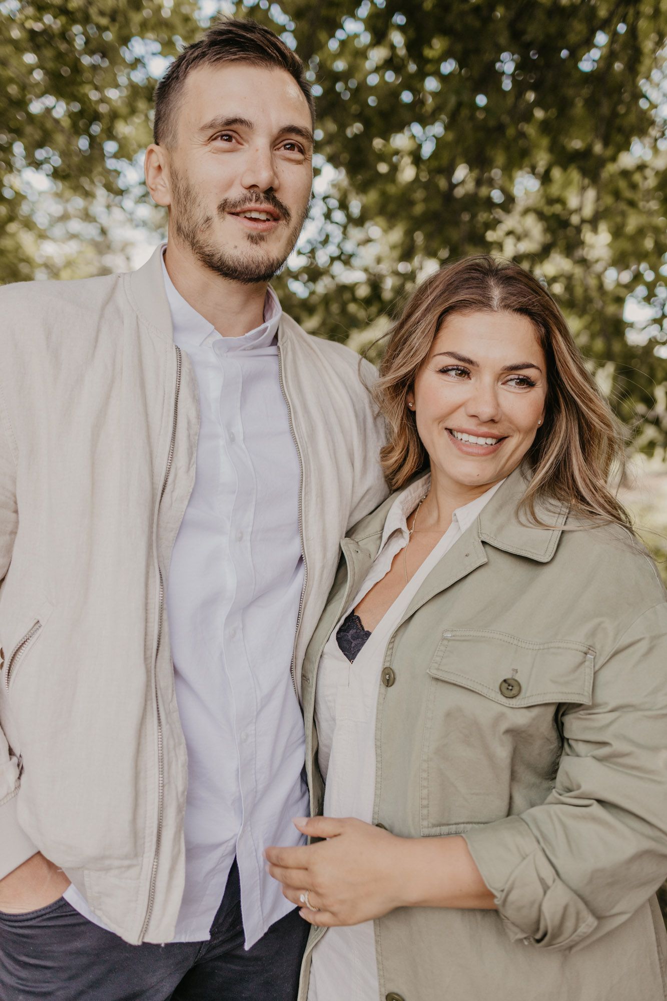 Outdoor portrait of stylish couple in light neutral jackets against natural backdrop.