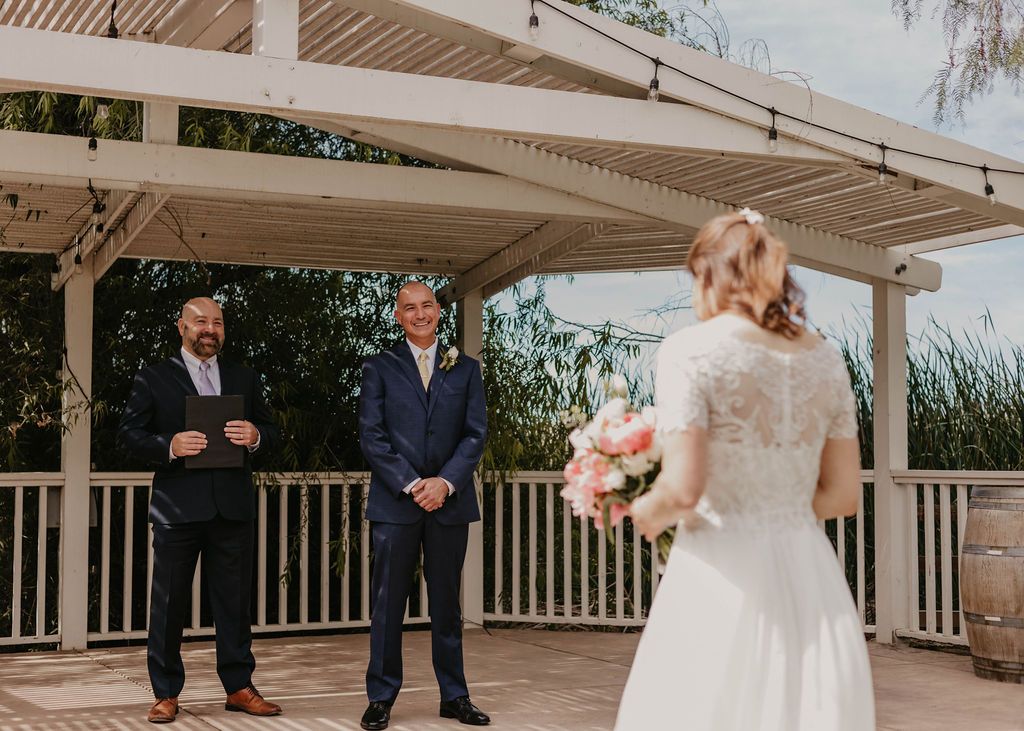 A wedding ceremony scene with two people standing before an officiant on a covered porch.