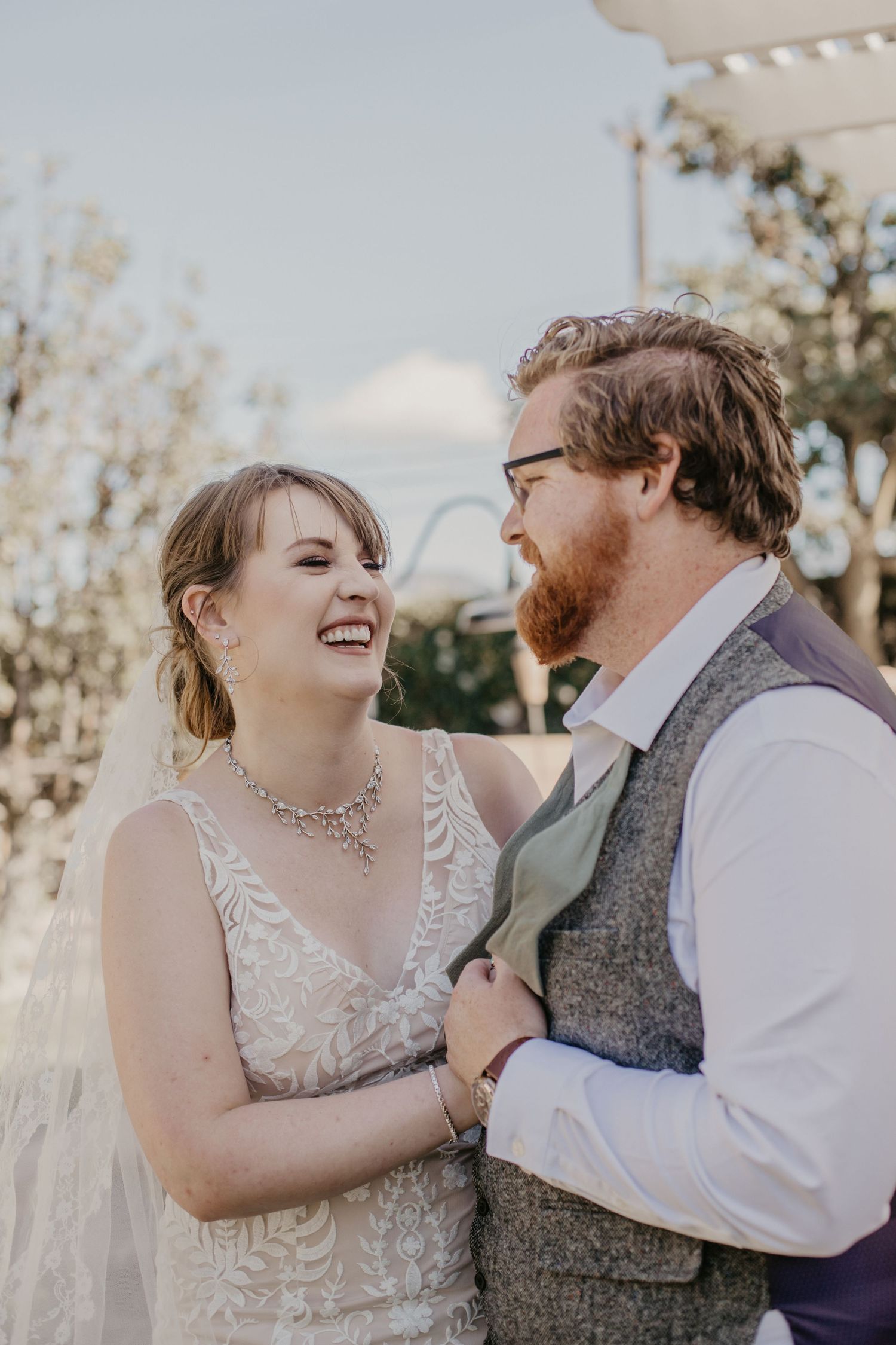 Joyful wedding couple sharing laughter during outdoor portrait session.