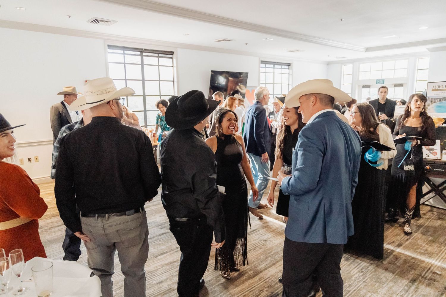 Guests mingle at an elegant indoor Western-themed event, with several attendees wearing cowboy hats in a bright venue.