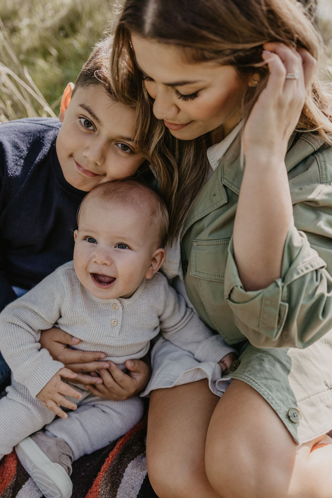 Intimate family portrait showing tender moments between siblings and parent outdoors.