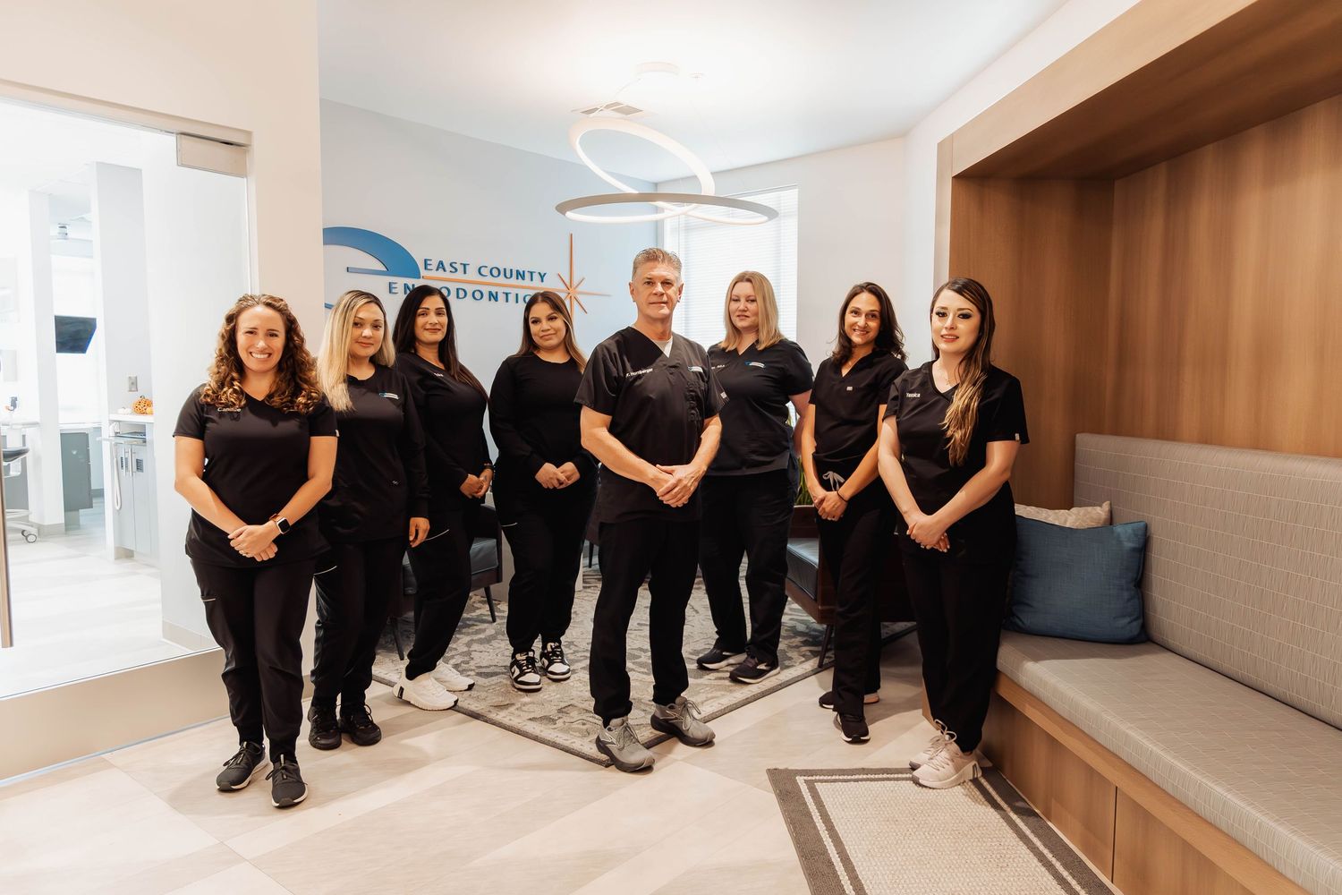 Group photo of team members wearing black outfits sitting together in a bright modern office space.