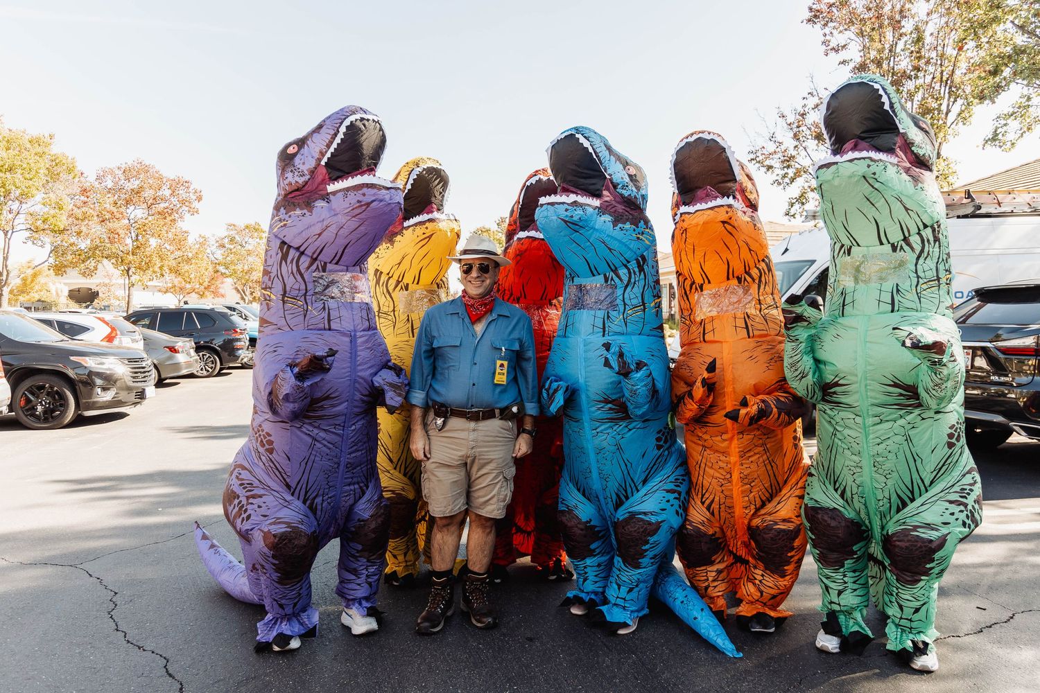 Group of people in colorful dinosaur costumes standing together outdoors.