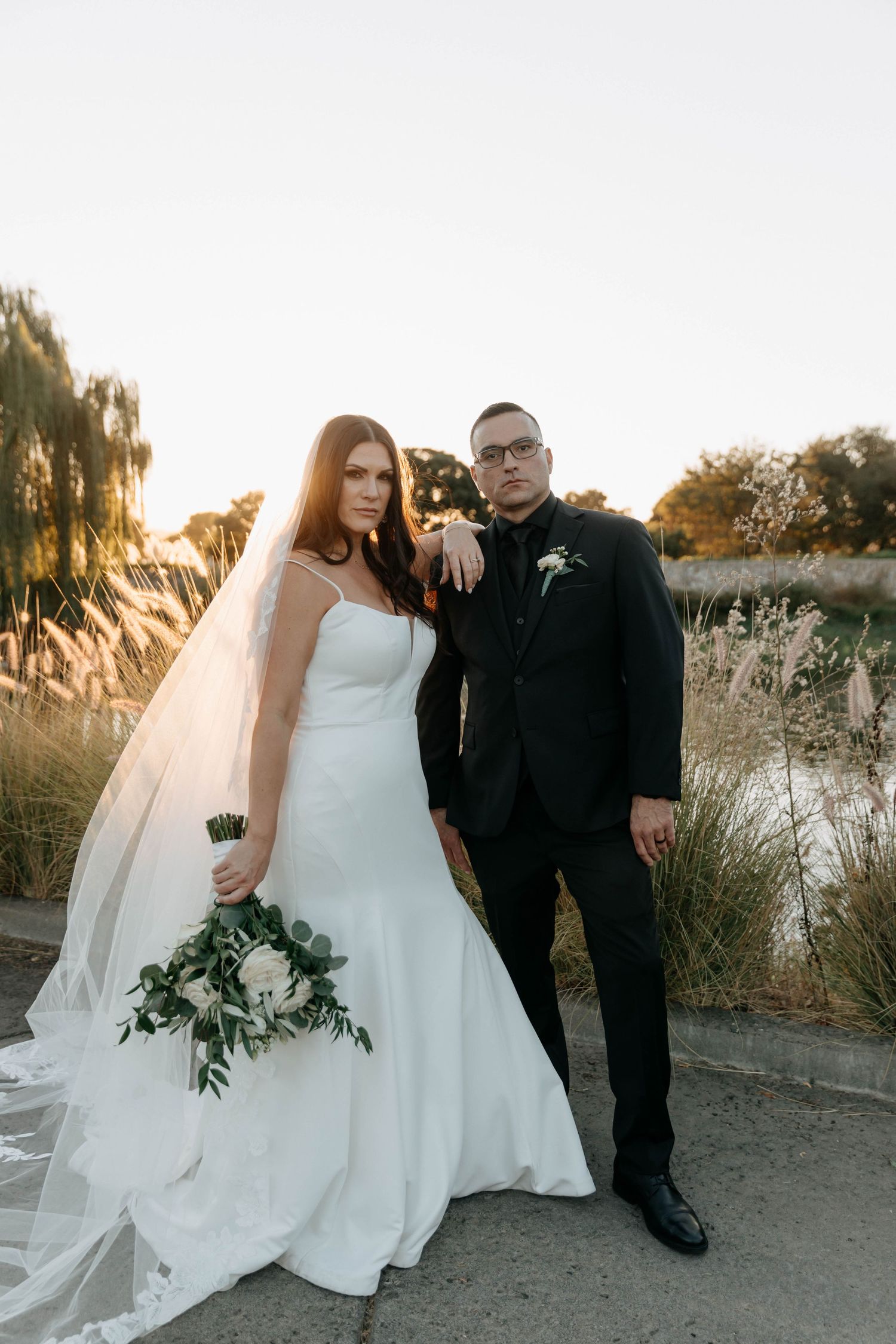 Sunset wedding portraits captured along a waterfront path with flowing white gown and veil.