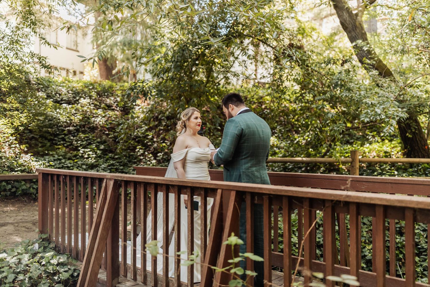 A couple walks along a rustic wooden bridge surrounded by trees and natural light.