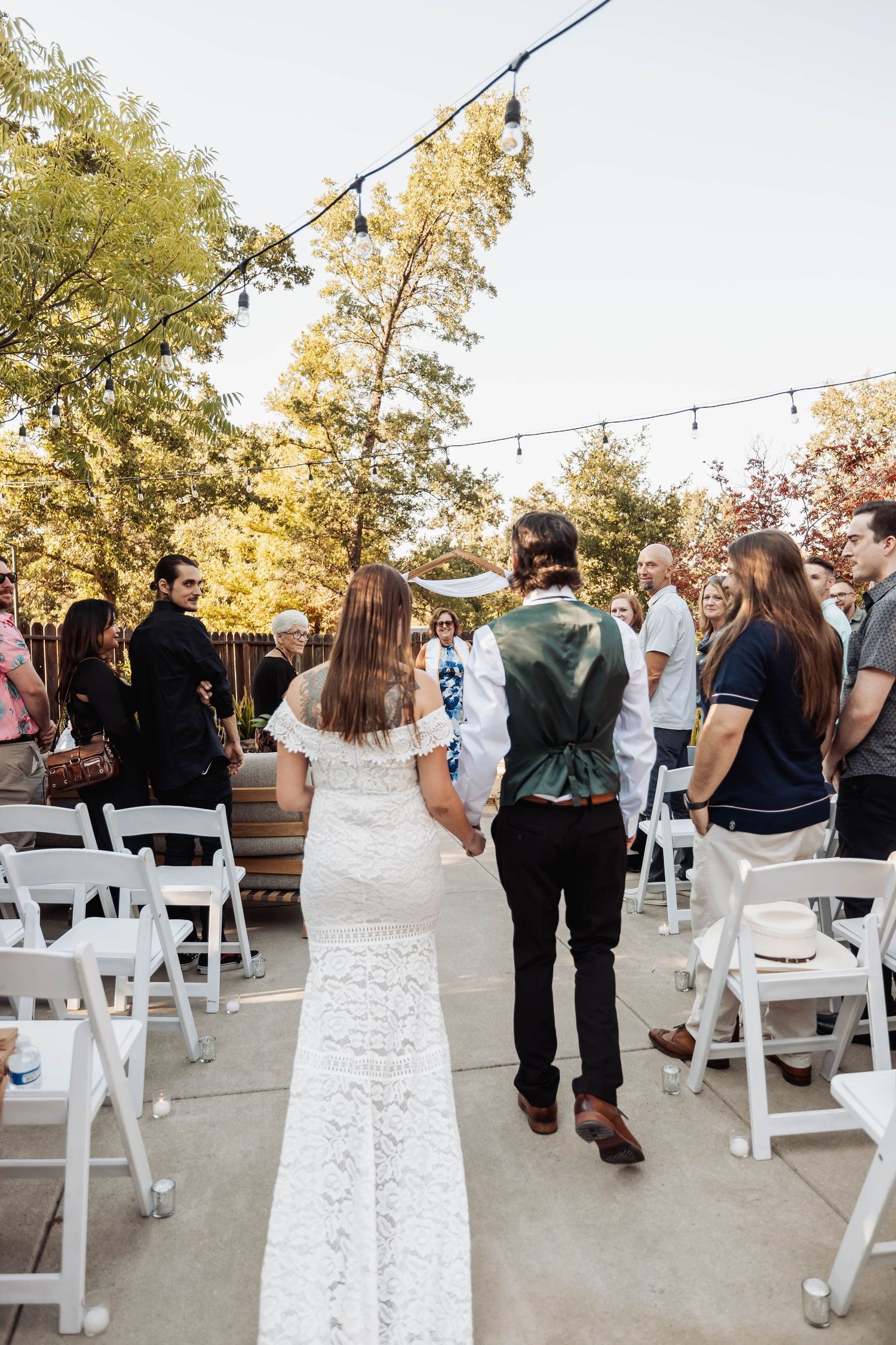 Wedding guests mingling around white chairs at outdoor reception venue.