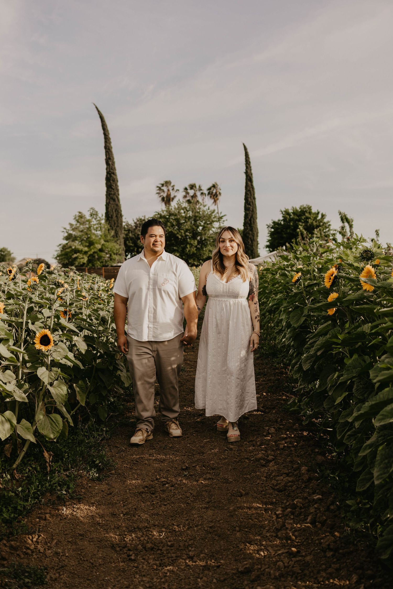 A couple strolls through a sunflower field during a golden hour photoshoot.