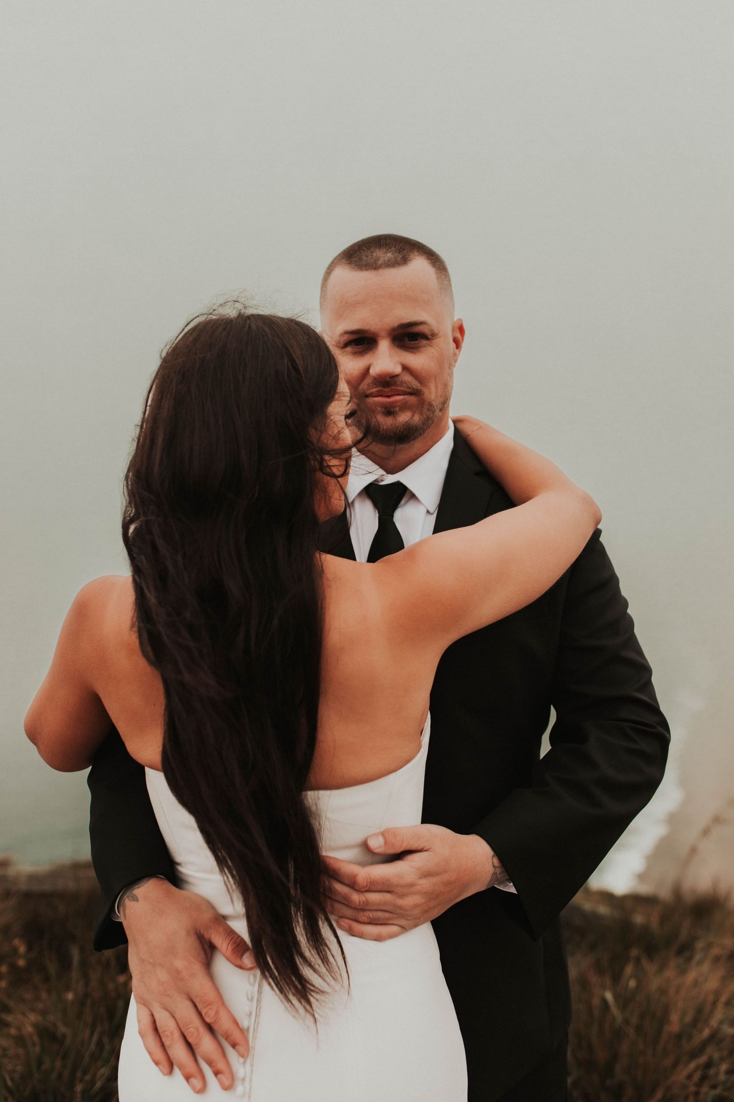 A tender embrace between newlyweds against a misty outdoor backdrop.