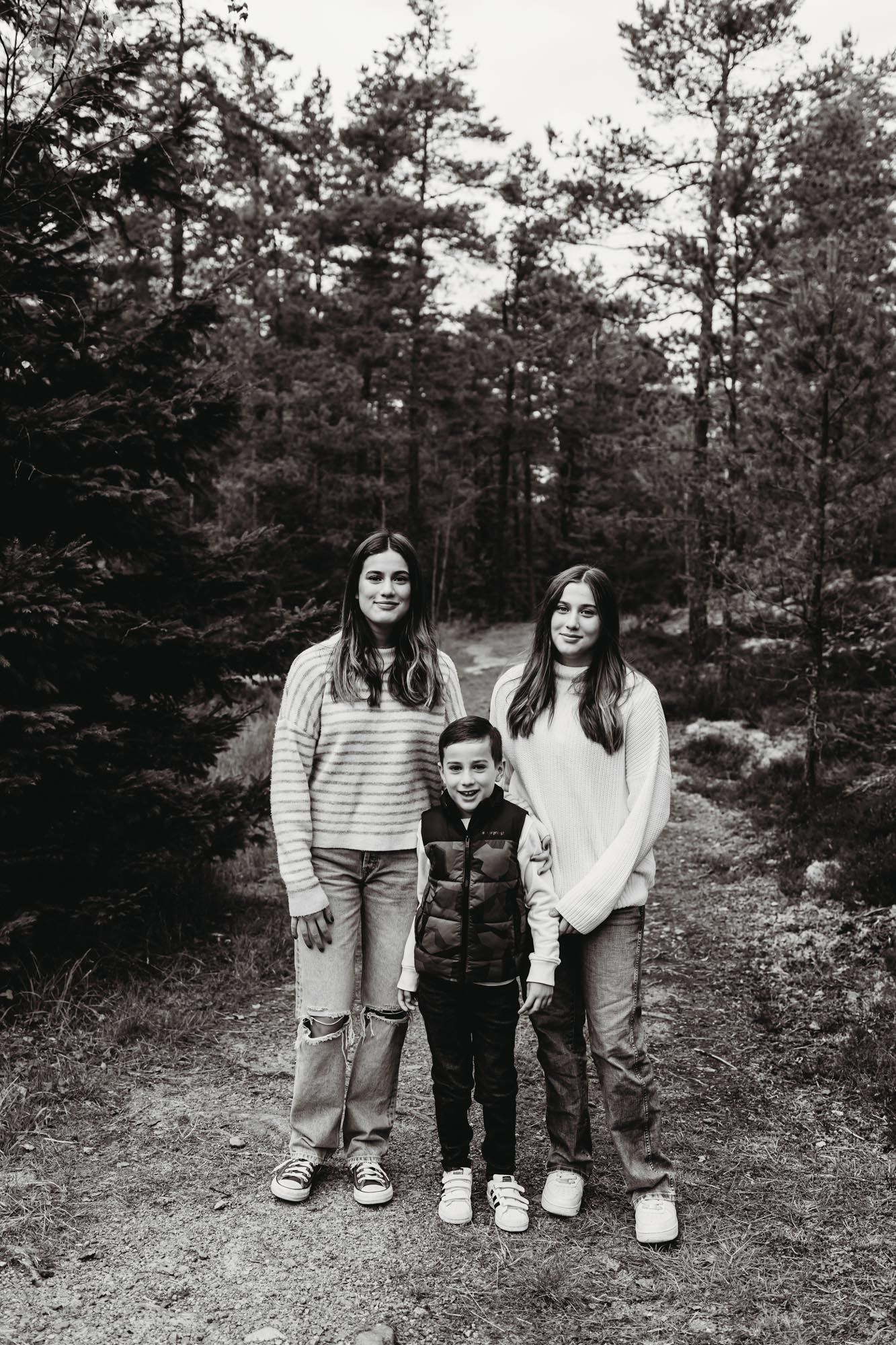 Three people standing together on a wooded trail in black and white photography.