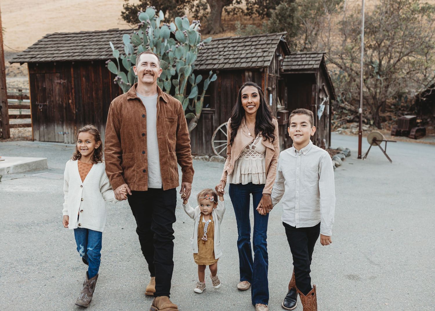 Family portrait with rustic cabin and large desert cactus in background.