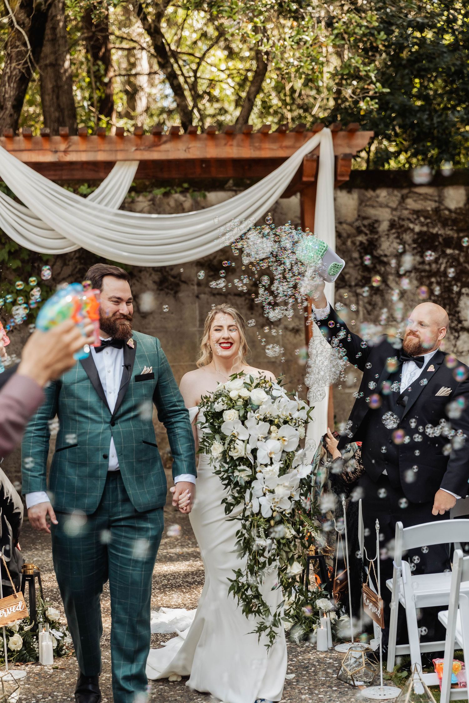 Wedding ceremony setup with white draping and floral arrangements under trees.