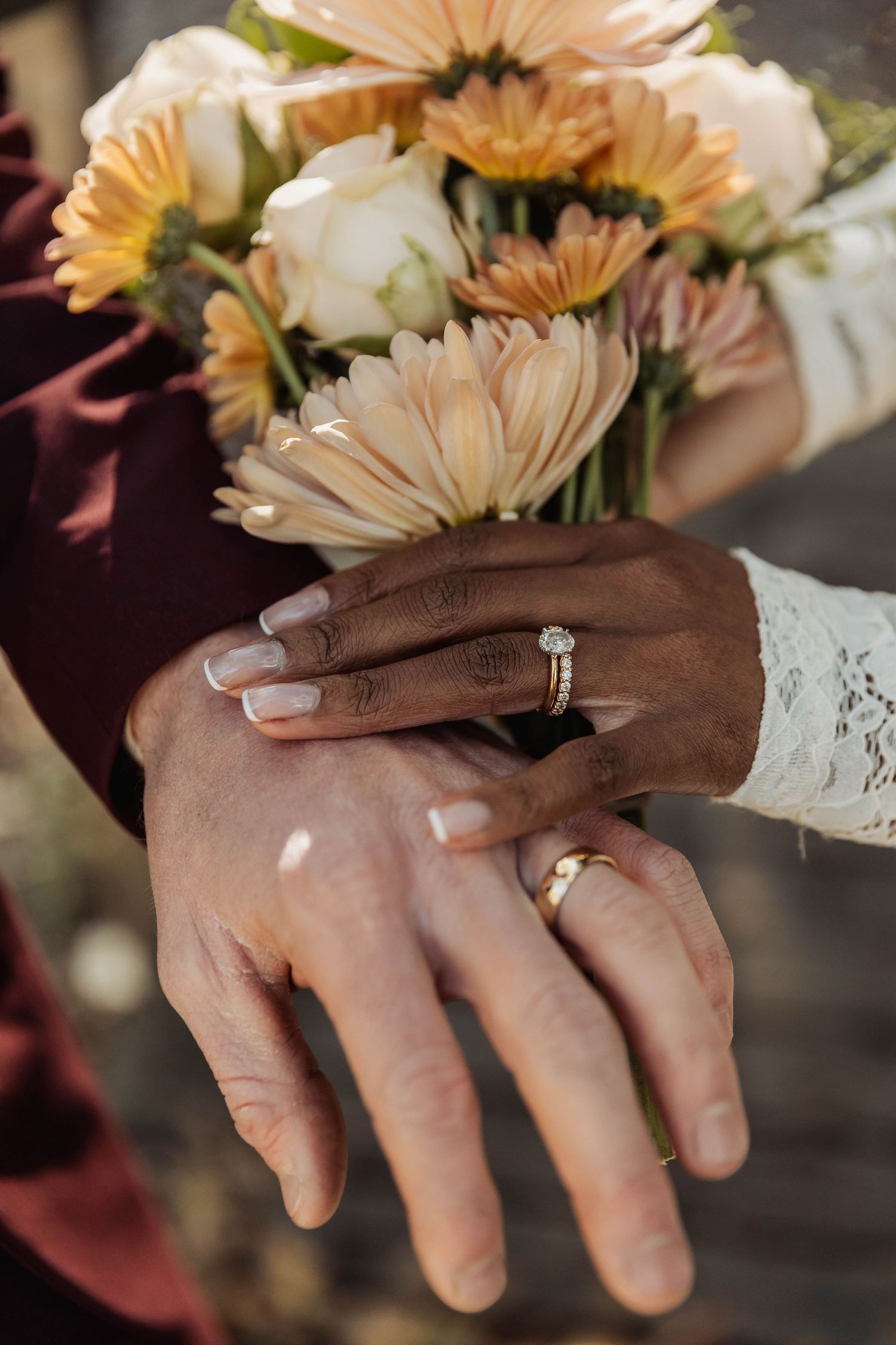 Close-up of hands with wedding rings and peach-colored flowers.