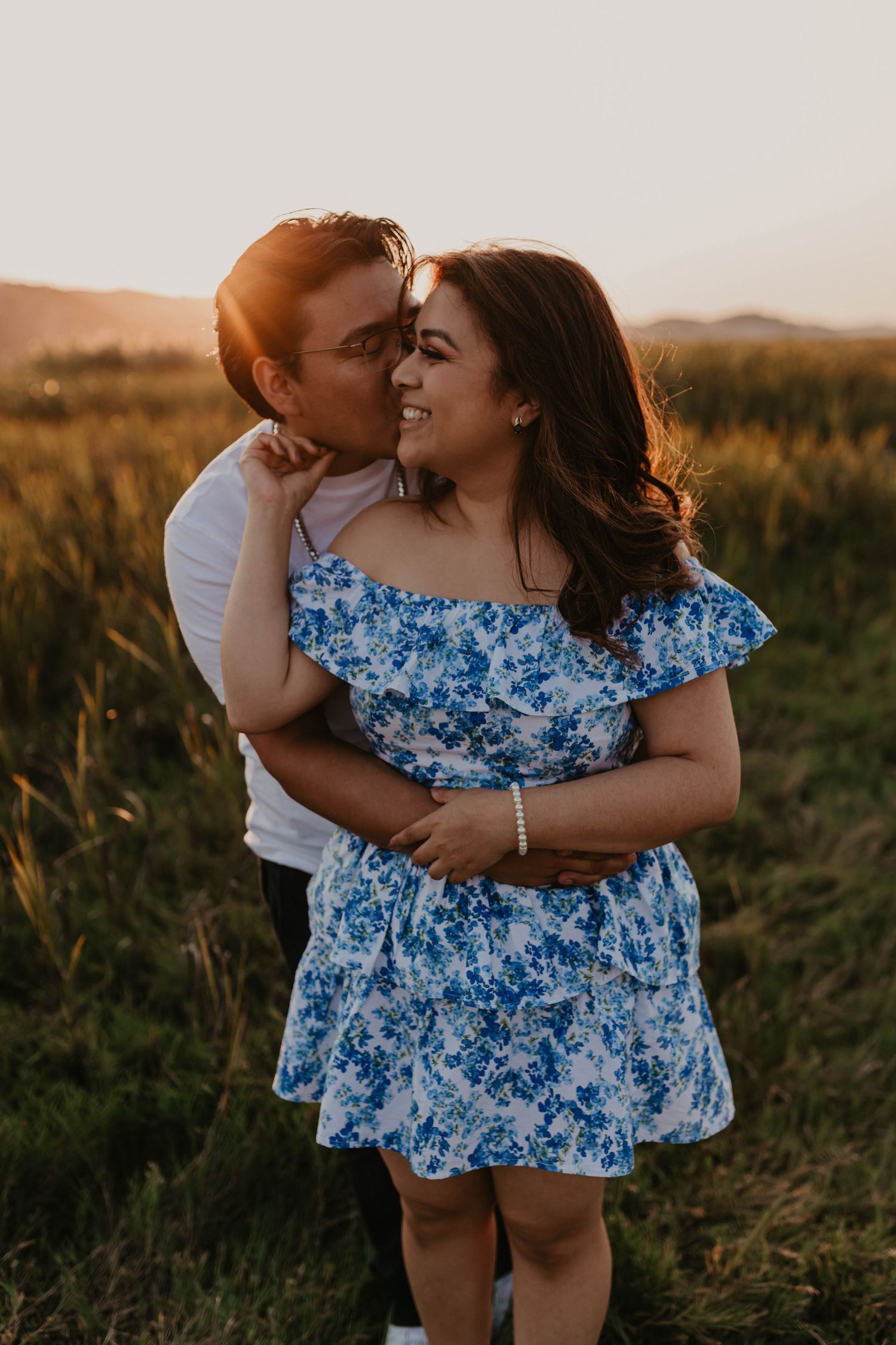 A tender moment captured between a couple in a blue floral dress and white shirt at sunset.