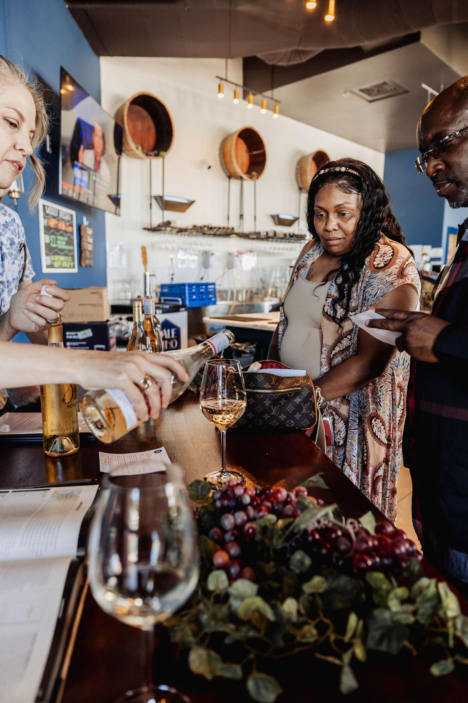 Wine tasting event at a bar with customers sampling wines and grapes displayed on the counter.