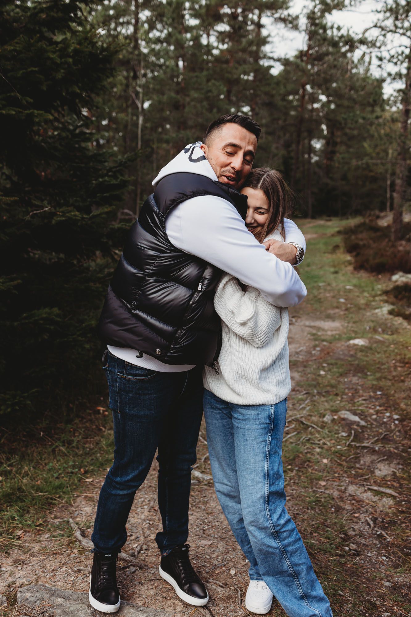 Sweet embrace shared between two people wearing winter clothing on a mountain trail.
