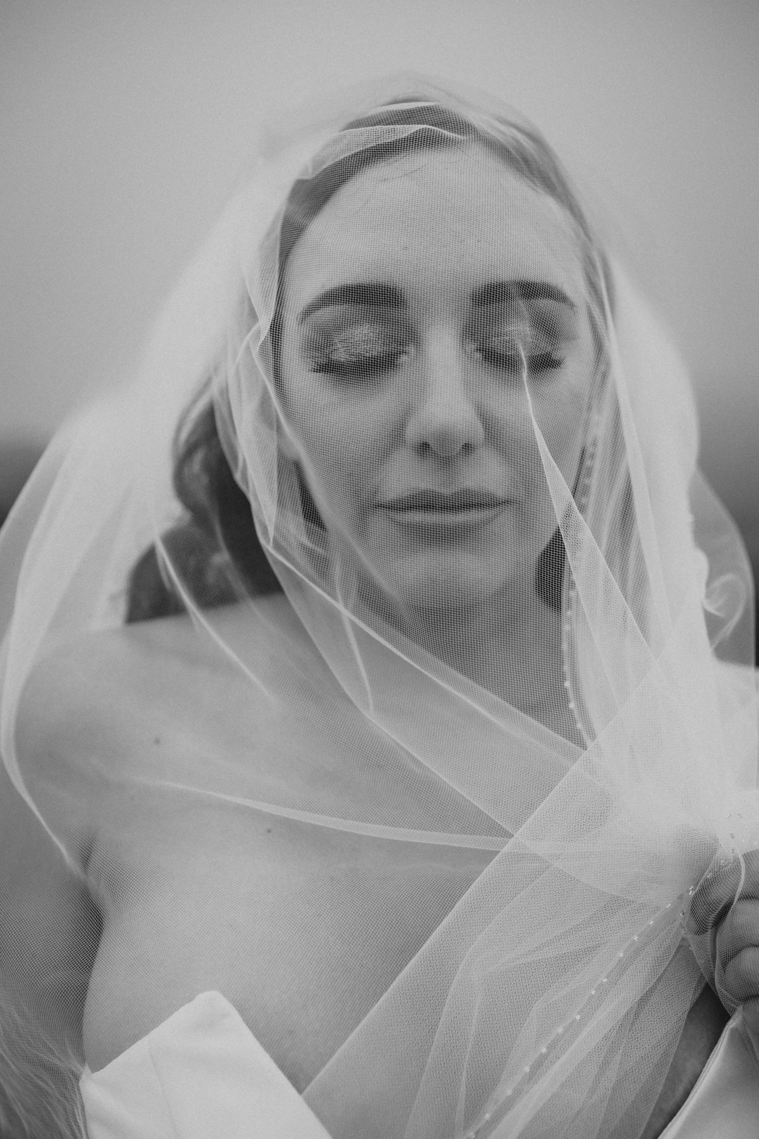 Artistic black and white portrait of a bride with eyes closed draped in sheer veil.
