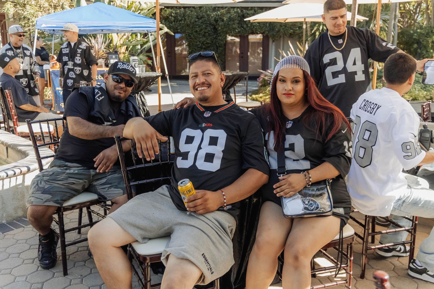 Group of Raiders NFL fans in black jerseys posing together at outdoor tailgate fan event.