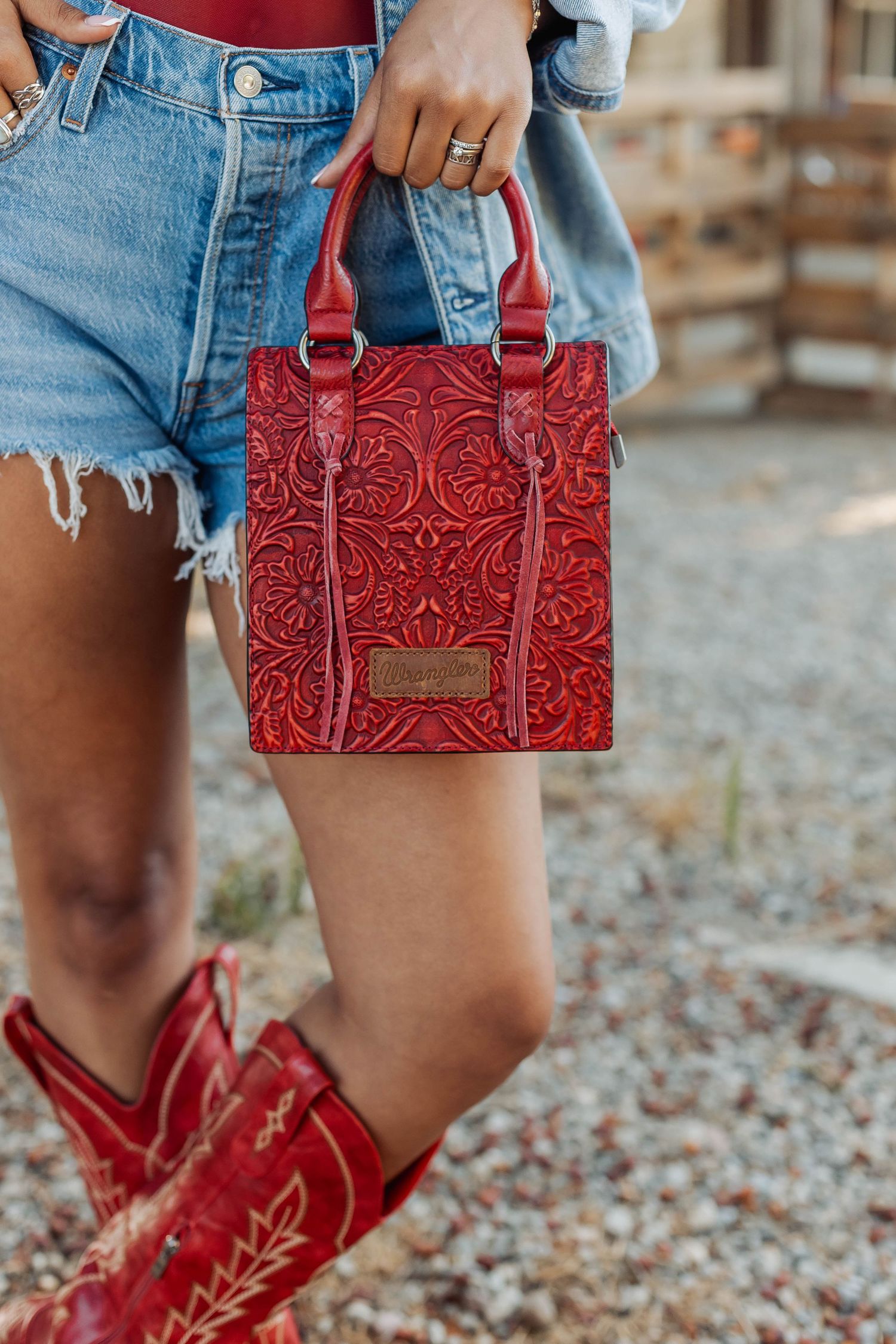 Red tooled leather handbag paired with denim shorts and red cowboy boots.