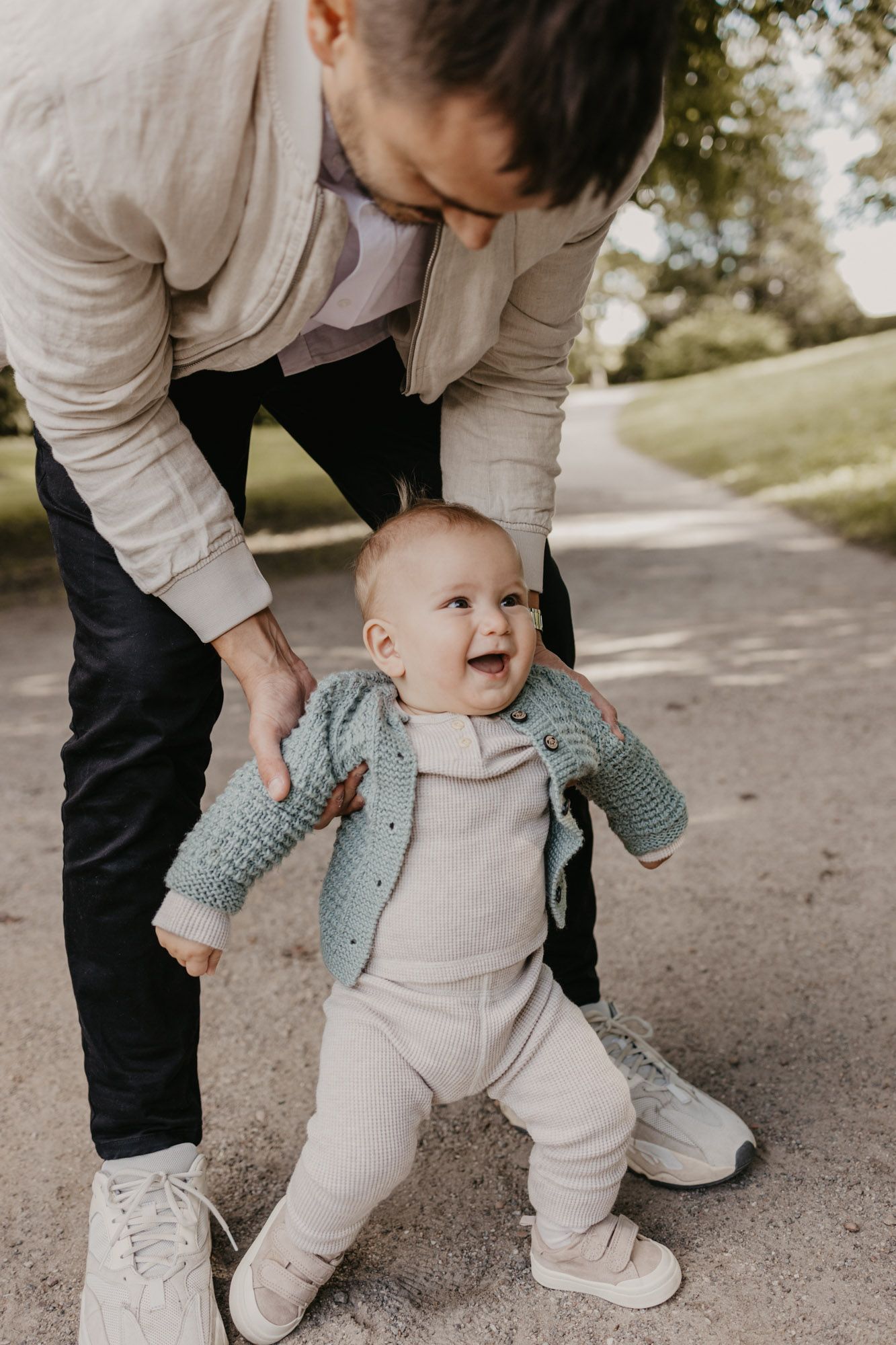 Touching moment of assistance with a baby learning to walk outdoors on a paved trail.