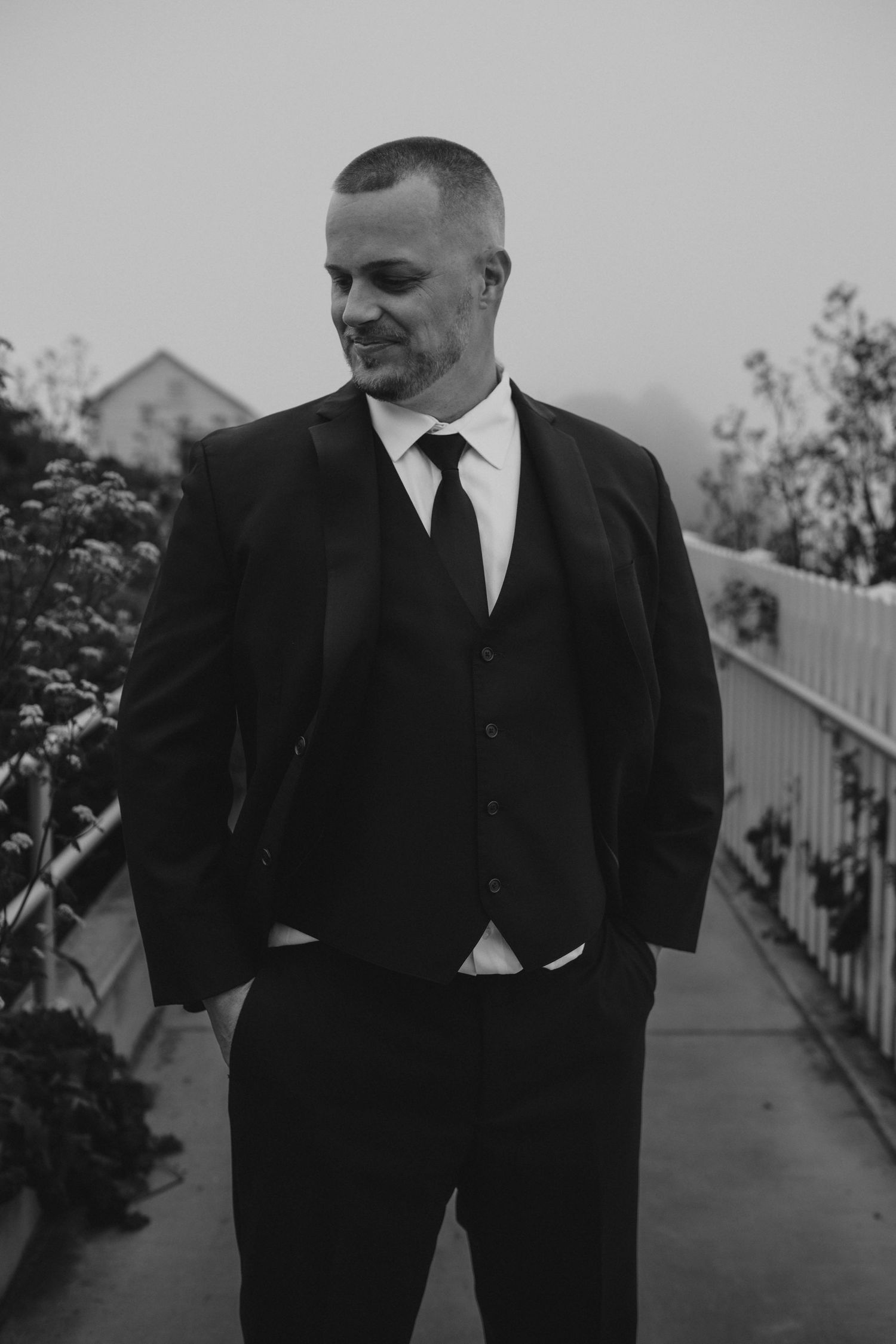 Black and white portrait of groom in classic suit on garden pathway.