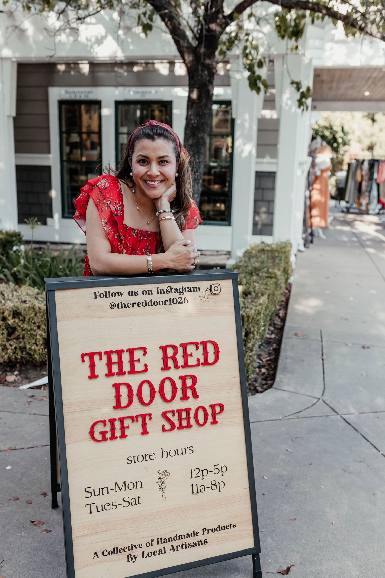 A person leaning on The Red Door Gift Shop business hours sign outside the storefront.