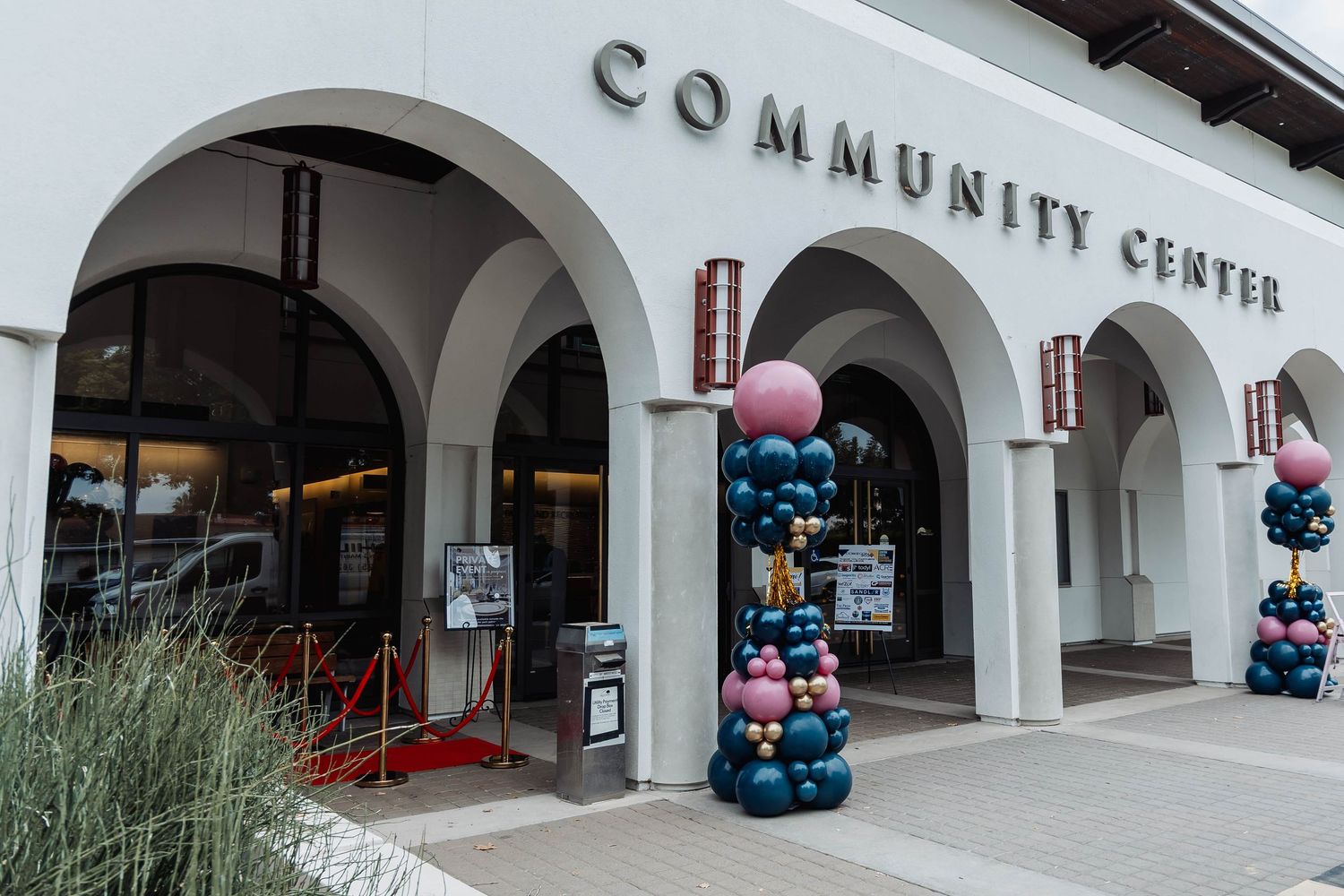 White arched exterior walkway of a community center decorated with colorful balloon arrangements.