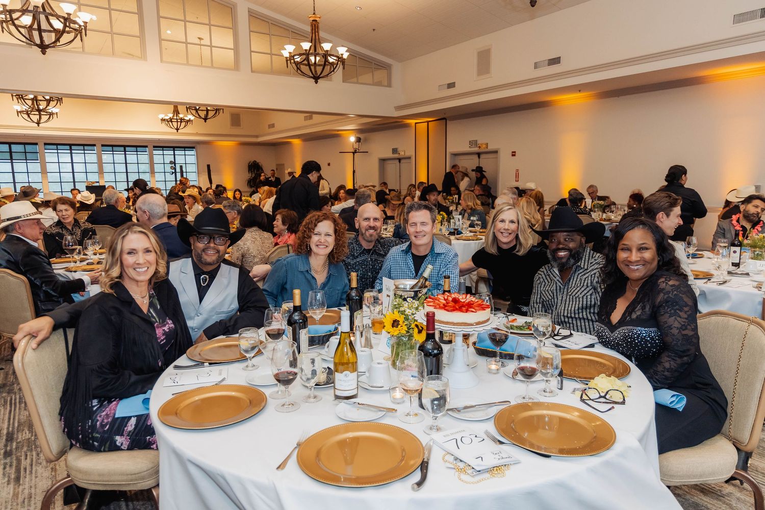 Diverse group of smiling guests seated at round banquet table during Grit & Grace charity fundraiser dinner.
