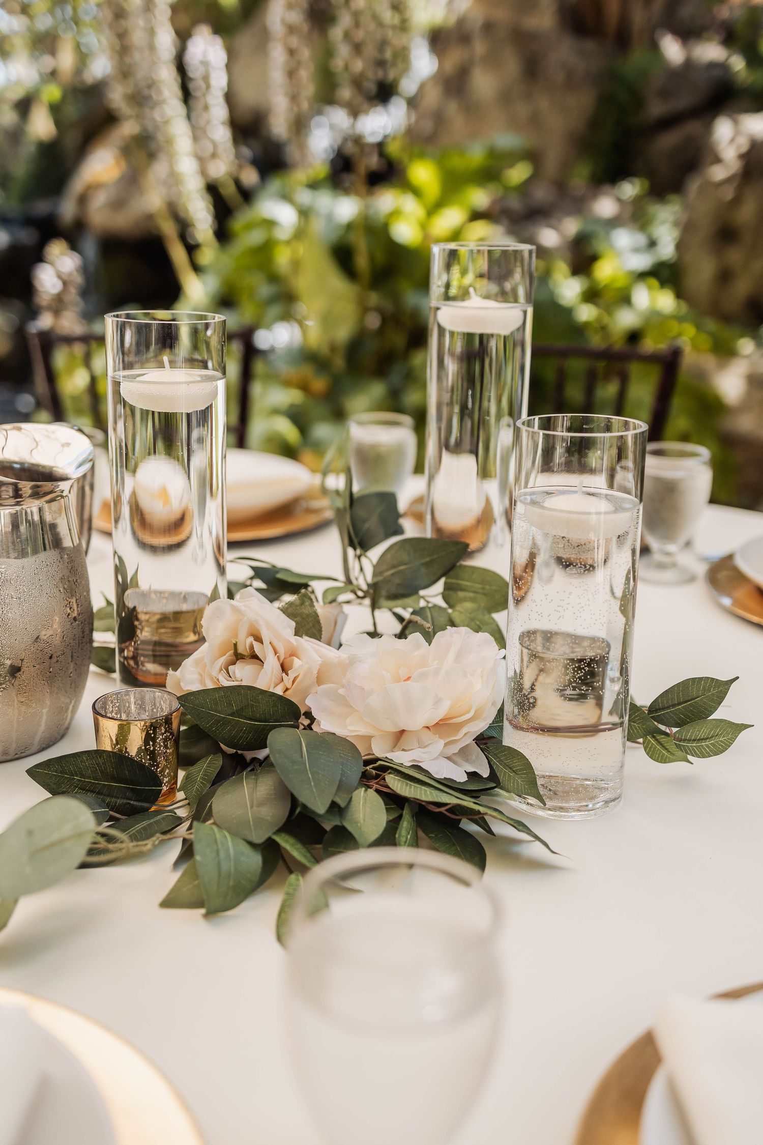Elegant wedding table decor featuring white candles, blush roses, and eucalyptus greenery on a crisp white tablecloth.