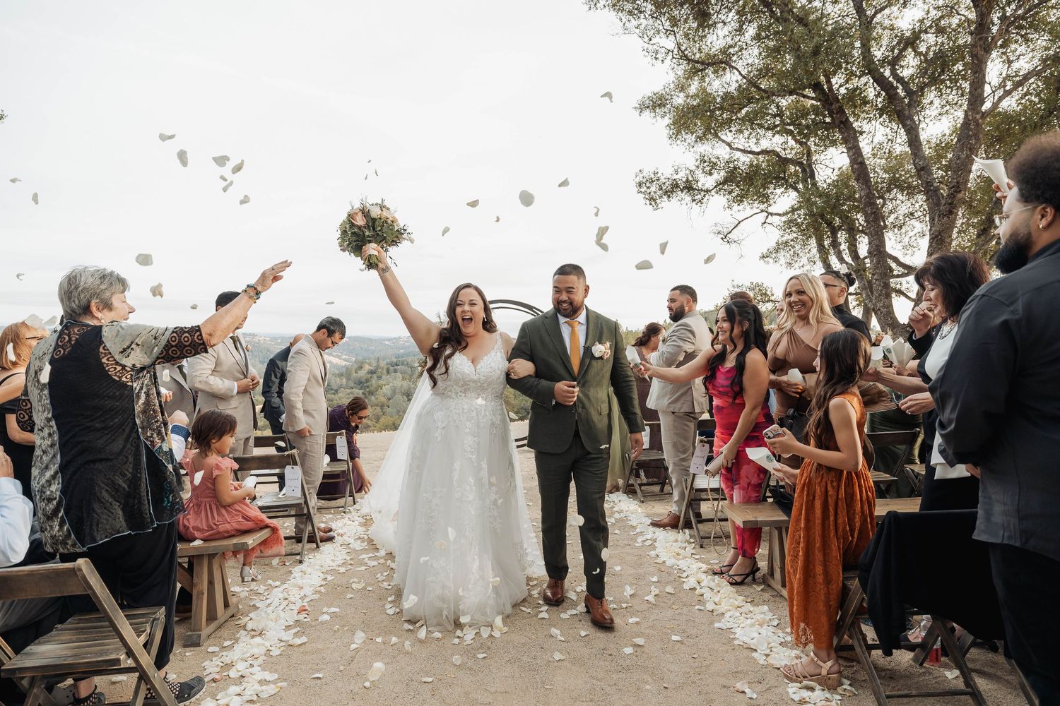 Wedding guests celebrate with confetti during an outdoor ceremony at sunset.