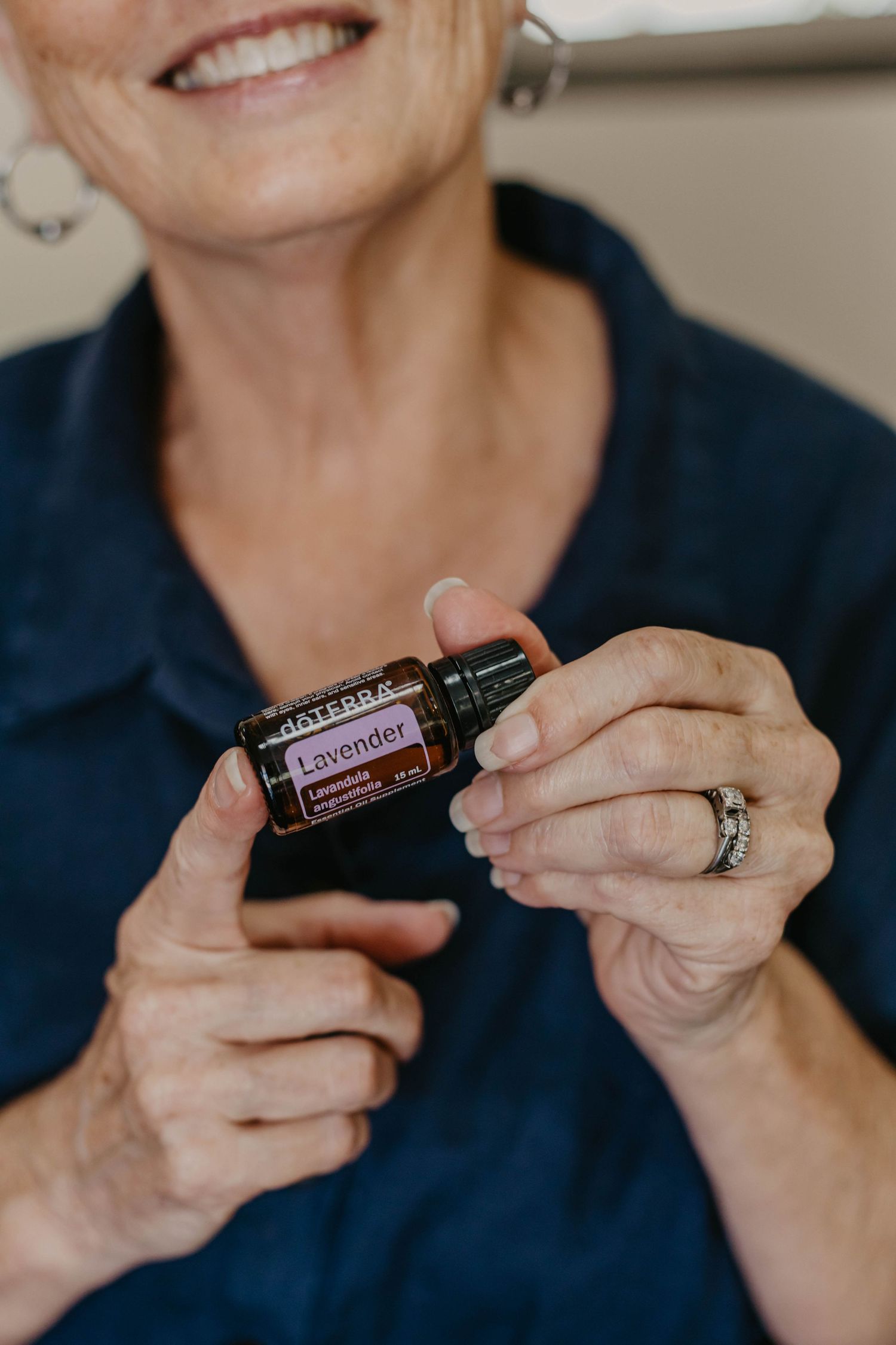 Close-up of hands holding essential oil bottles against navy blue clothing.